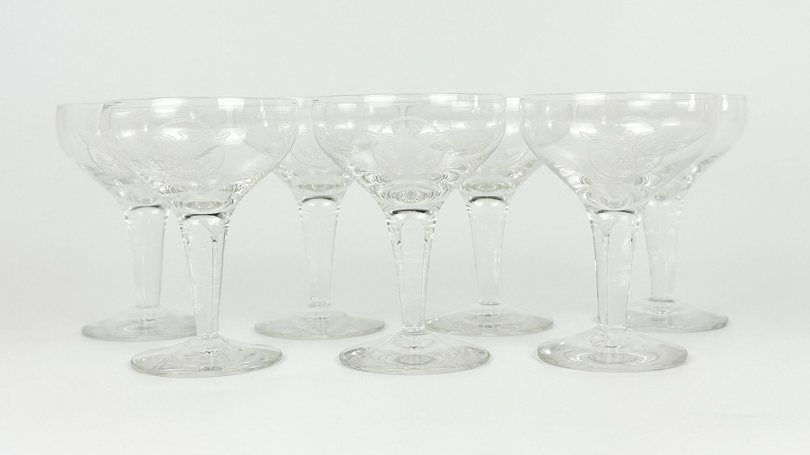 SS United States Cocktail Glasses w/ US Lines Eagle Logo (7): 7 Cocktail glasseswith etched US Lines eagle logo. Dimensions: Each glass is approx. 4in H x 3in W. Weighs 1 lb7 oz.