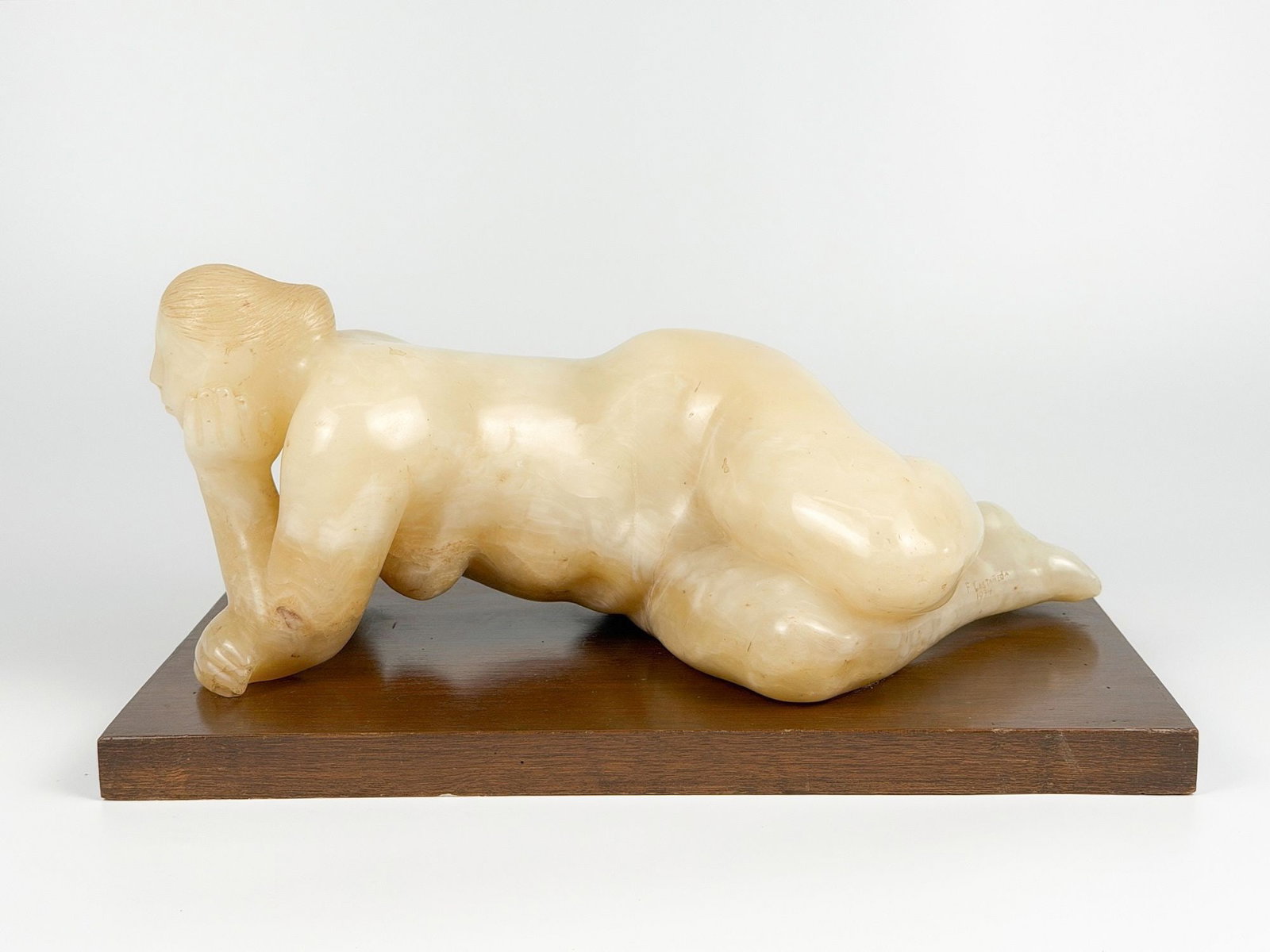 Felipe Castaneda (b. 1933) White Onyx, Reclining Nude, 1974: Signature engraved onto inner right ankle. Depicts carved stone female nude mounted onto a wooden slab. Dimensions: Approximately 7.5 in H x 15.75 in W x 8.5 in D. Weighs approximately 22 lbs 10 oz. L
