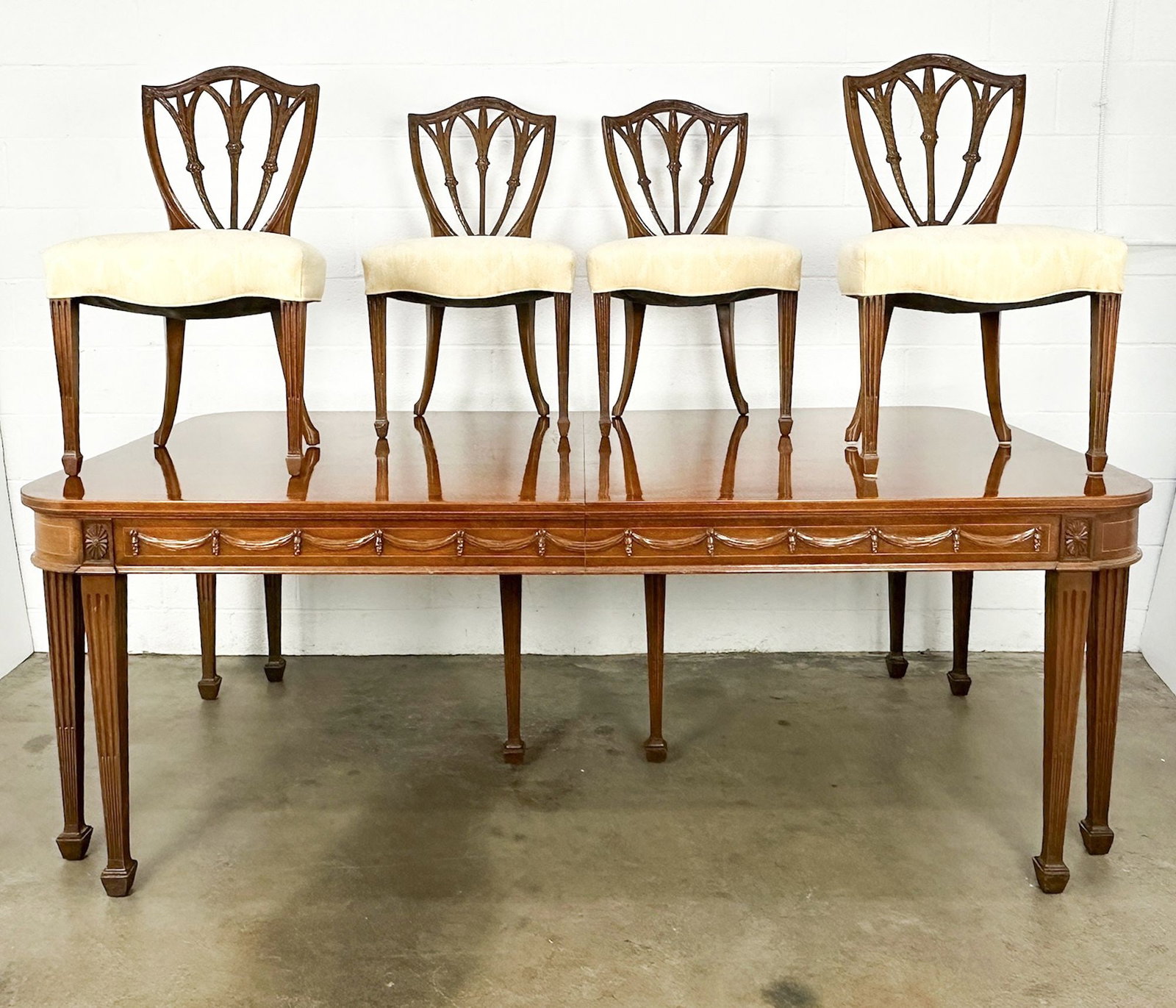 Joseph F. Milbeck Federal Style Dining Table, 4 Chairs and 4 Leaves: Inlaid wood on edges. Burlwood veneer w/ carved accents along edge of table. Carvings on backrest of chairs. Dimensions: Table without leaves is approx. 31 in H x 84 in W x 45 in D. Table w leaves is 