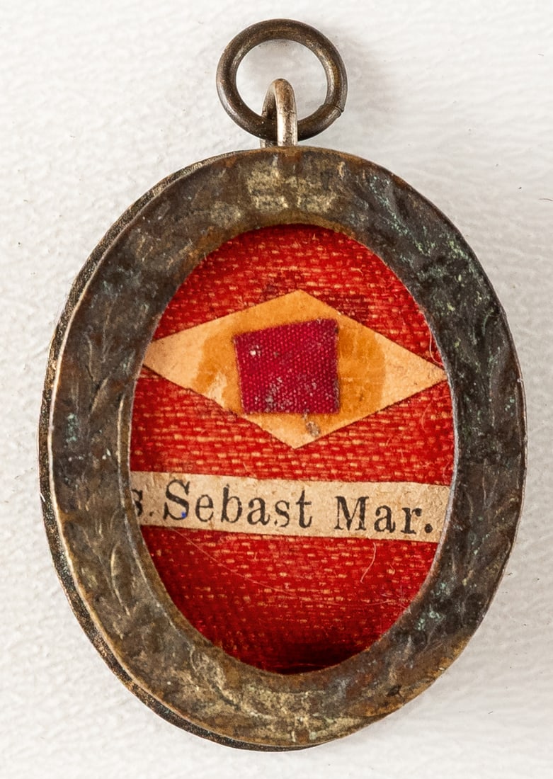 CAPSULE WITH RELIC OF ST. MARTYR SEBASTIAN: Oval metal pendant, unglazed, containing a relic with a ribbon underneath. The reverse depicts the Virgin Mary in profile. probably early 20th c. 2.6 x 2.3 x 0.8 cm