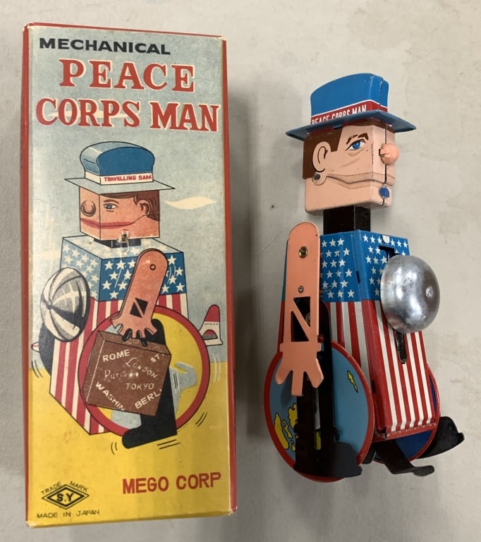 JOHN KENNEDY INSPIRED LITHO TIN WINDUP TOY BY MEGO: Box and toy about 2.5x3x7" tall. Tiny puncture on box lid but rest of box is Exc. Toy needs a spring repair in order to work but paint is near mint. His hat reads "Traveling Sam / The Peace Corps Man.
