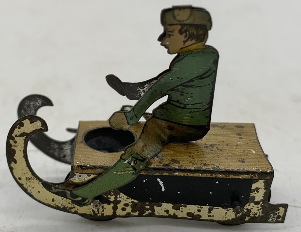 tin penny toy boy on sled: has wear with scratches and paint loss