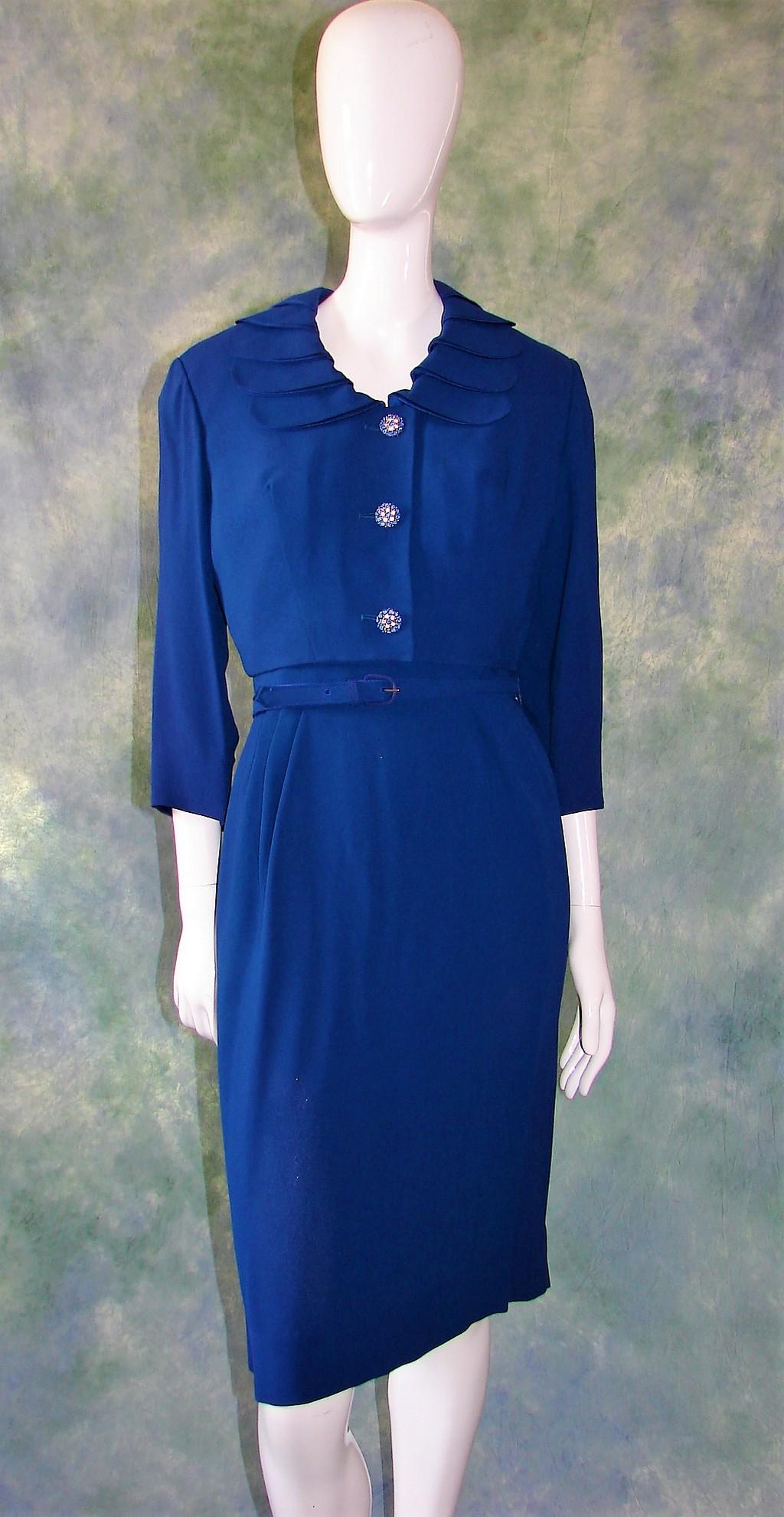 1960s Ladies Two Piece Blue Crepe Dress and Jacket: Dress has beautifully constructed neckline finished with small crepe bows creating pleats in the shoulders, darts in bust, pleated waist, slanted sleeves, darts in back. Measures 40" long, 26" waist, 