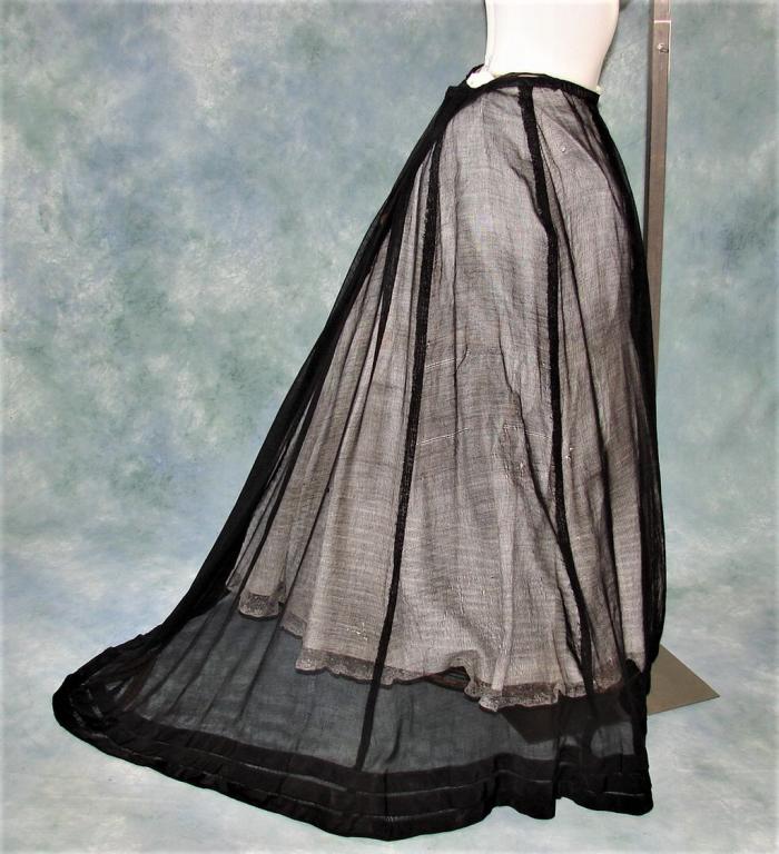 Edwardian Ladies Black Net Trained Bustle Ski: Black netted skirt with three silk self flounces at hemline, silk waistband closes with three hook and eyes, measures 28" w x 39" long in the front and 51" train, 52" h