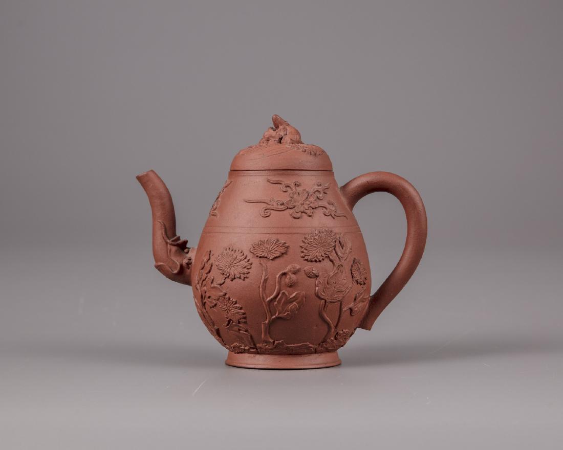 A Chinese yixing floral appliqué teapot and cover: The body is decorated with sprig-moulded chrysanthemum amongst rocks below flower sprays with curling tendrils. The spout emanates from a dragon head and the cover is decorated with a squirrel and gra