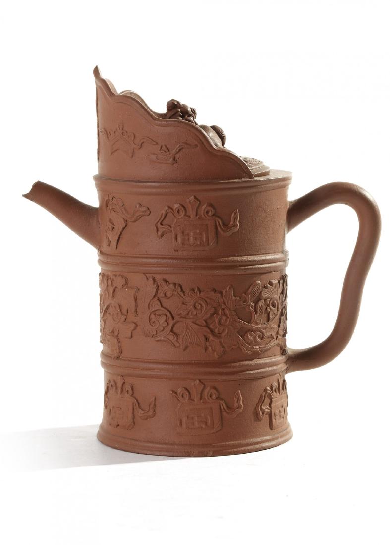 A Chinese yixing 'monk's cap' teapot: The teapot is modelled after a Buddhist ewer crafted from metal, the cylindrical body is separated into three sections decorated with applique auspicious symbols separated by a band of scrolling flowe