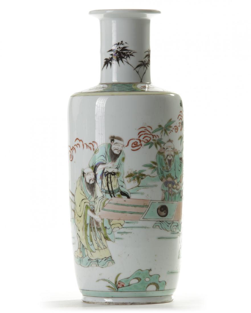 A Chinese famille verte 'scholars' rouleau vase: The vase is decorated with five scholars admiring a painting beside a flowering tree on a terrace in a mountainous landscape. The shoulder is decorated with a diaper band with cartouches enclosing pre