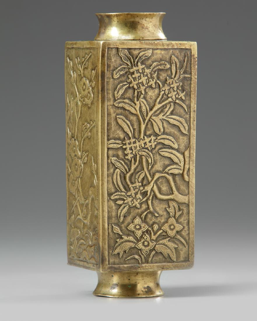 A Chinese bronze 'floral' square-section vase, cong: The vase is crafted of rectangular section and circular flaring neck and foot, each flat side is decorated in low relief with a different flower Â– camellias, roses, osmanthus, and chrysanthemum on