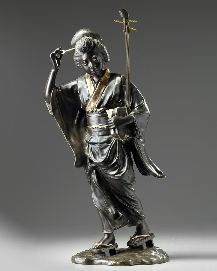 A Japanese gilt bronze lady figure: A bronze cast of a lady wearing a partial gilt kimono and holding a music instrument, with a comb in her hair and standing on an oval stand. Of Tokyo-school Meiji period around 1900. Origin: Japan Per