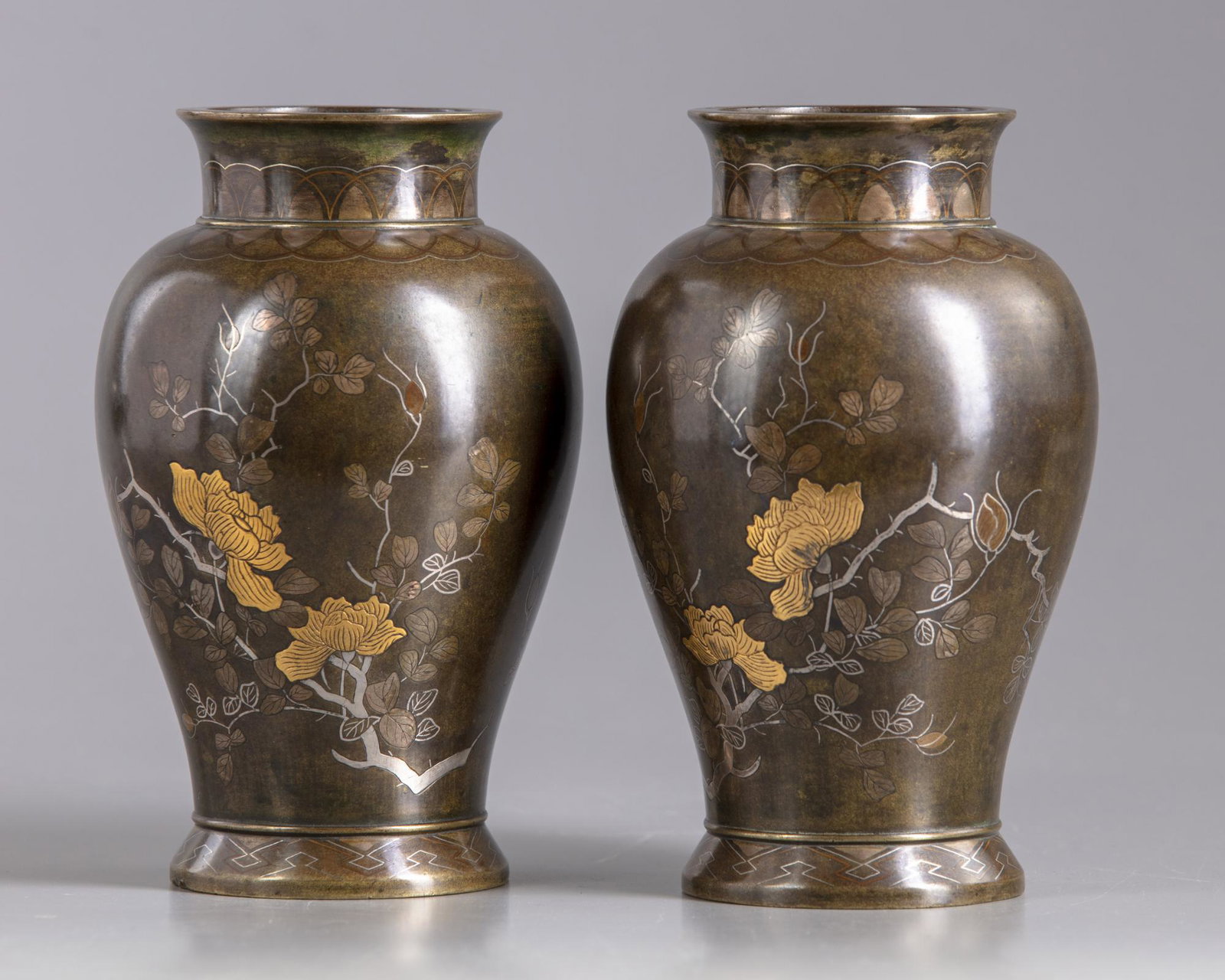 A pair of Japanese bronze vases: Two Japanese bronze vases, with flaring base and waisted neck, carved in low relief and inlaid in silver, gold, with a butterfly flying over flowering branches. Origin: Japan Period: Meiji period (186