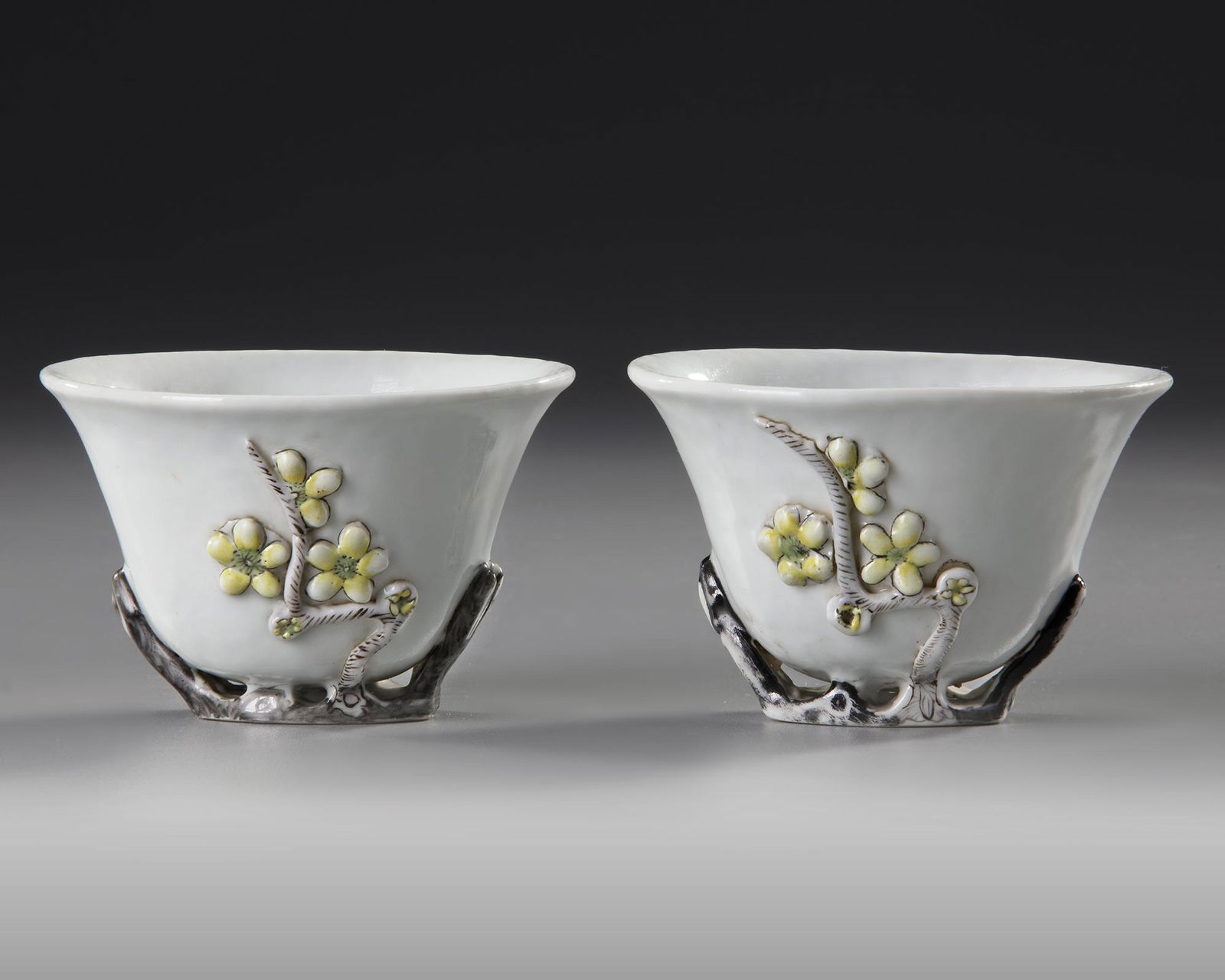 A PAIR OF CHINESE BLANC DE CHINE WINE CUPS, 18TH CENTURY: The white cups decorated on both sides in relief with magnolia-blossoms, each polychromed with yellow and red enamels. The cup is supported on the underside with the flower branch and enamelled in bla