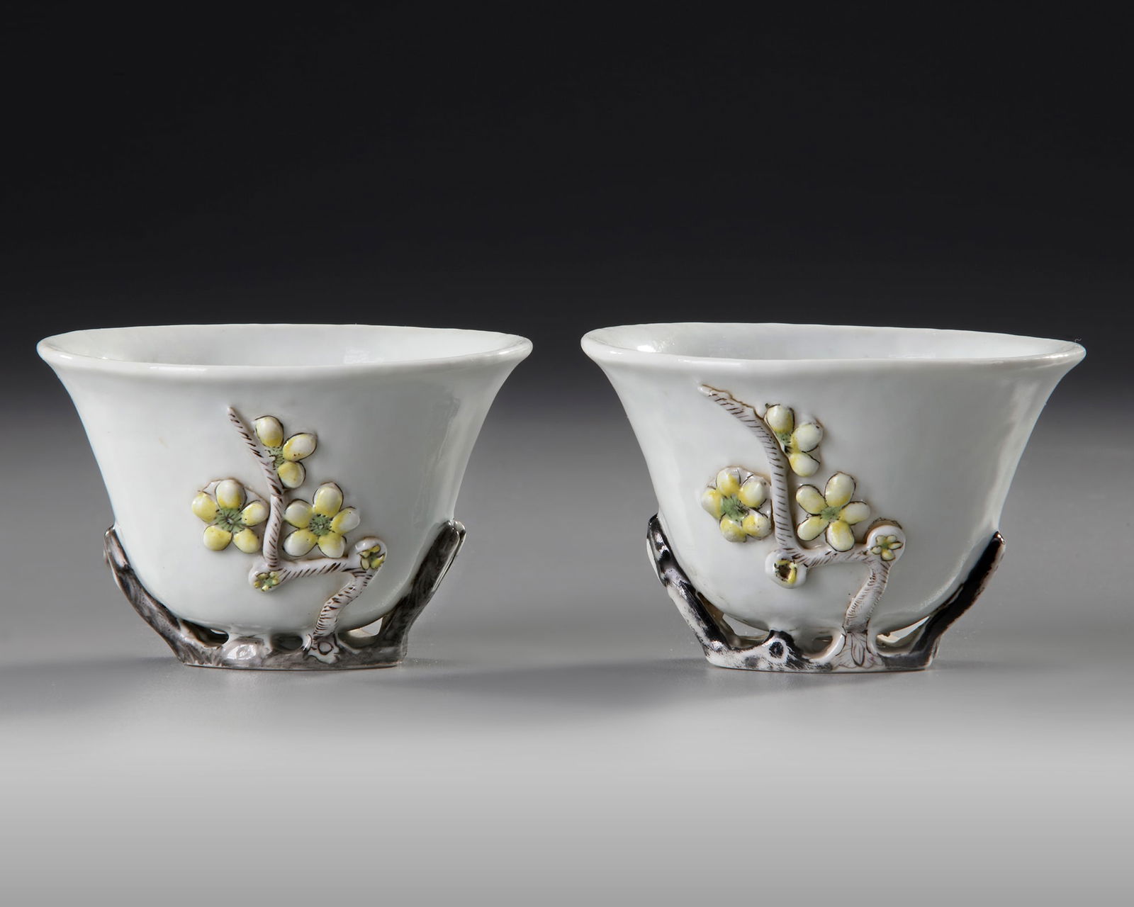 A PAIR OF CHINESE BLANC DE CHINE WINE CUPS, 18TH CENTURY: The white cups decorated on both sides in relief with magnolia-blossoms, each polychromed with yellow and red enamels. The cup is supported on the underside with the flower branch and enamelled in bla