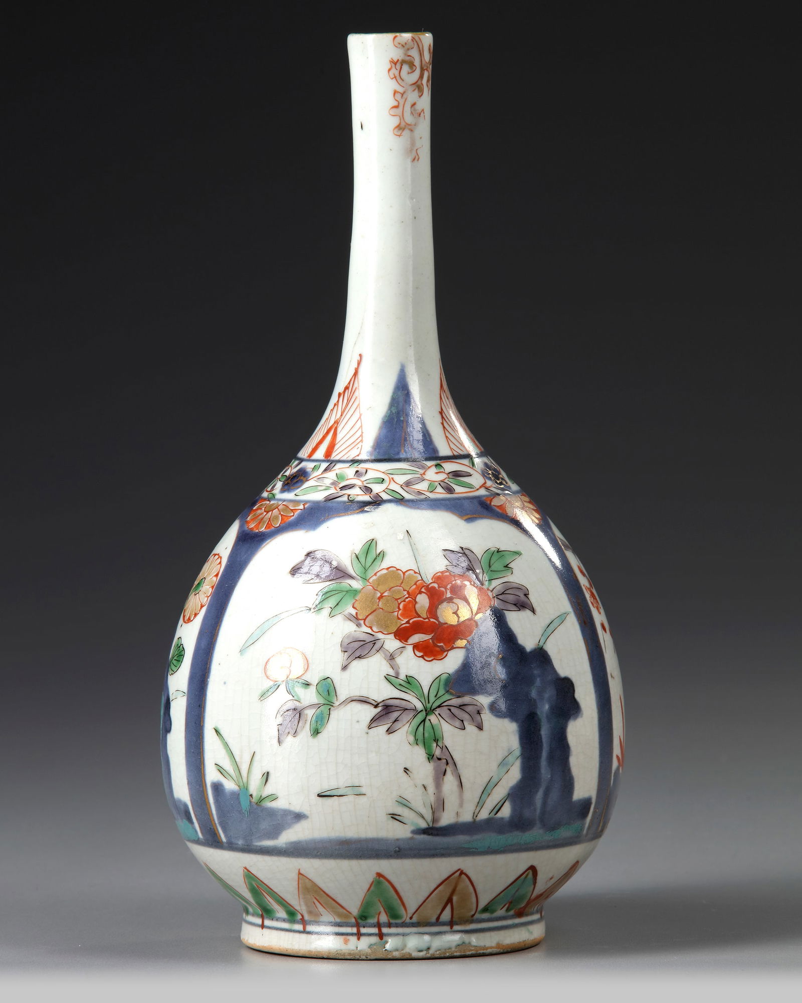 A JAPANESE IMARI BOTTLE VASE, EDO PERIOD CIRCA 1700: Japanese imari bottle vase, Edo period, circa 1700, decorated with three panels containing cherry blossom, bamboo and other flowers issuing from rockwork, below a band of scrolling foliage decoration.