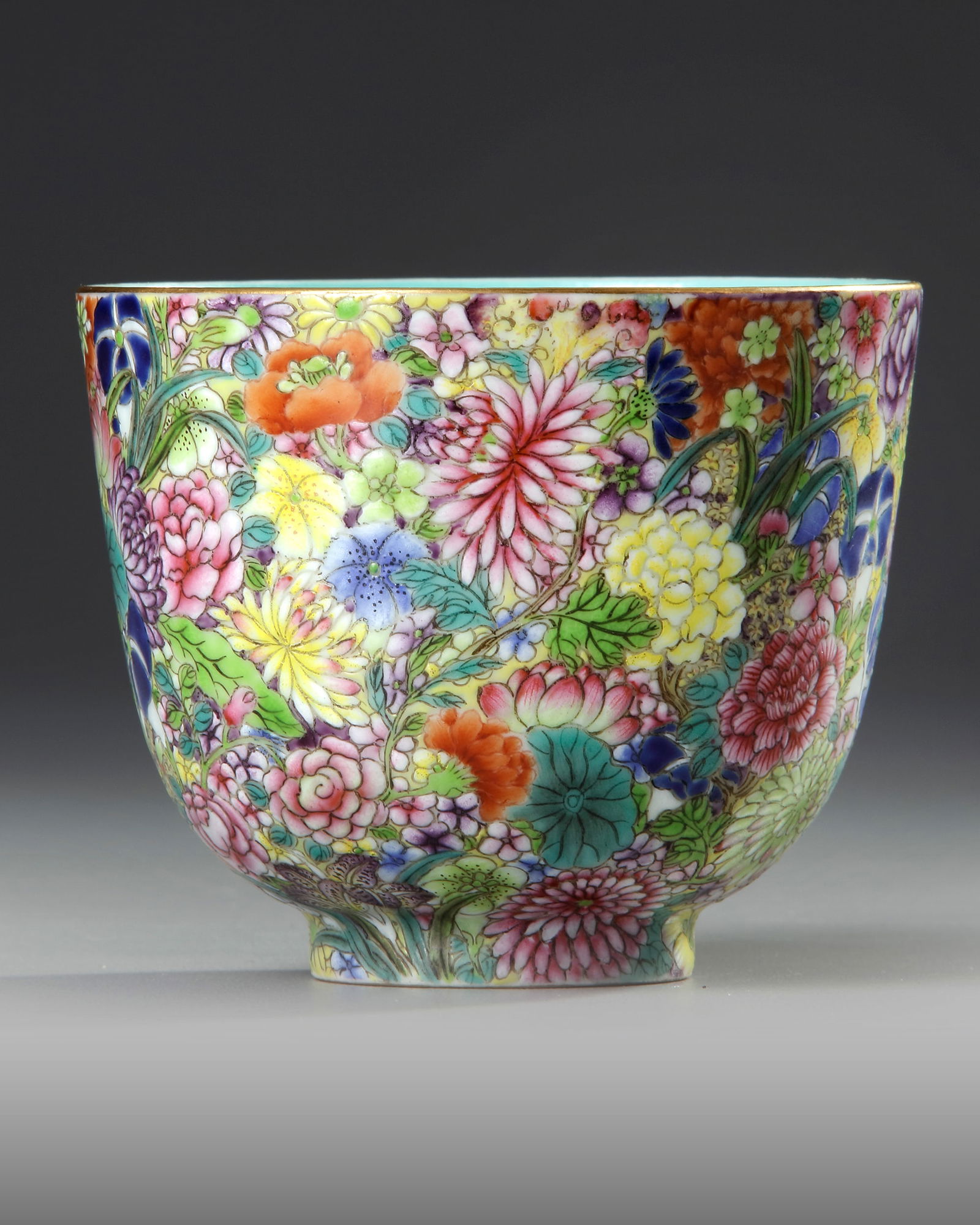 A CHINESE FAMILLE-ROSE 'MILLE-FLEURS' CUP, 19TH-20TH CENTURY: A Chinese porcelain cup with small foot and deep sides, decorated on the exterior with a dense pattern of various flowers below the gilt mouth. The bottom with a Chinese Jiaqing seamark in iron-red on