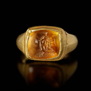 A BYZANTINE GOLD RING WITH A TOPAZ INTAGLIO WITH A BUST OF CHRIST, 6TH/7TH CENTURY AD: A Byzantine gold ring made of repousse sheet with a square topaz intaglio showing the bust of Christ with a cross shaped nimbus. The ring itself is made of thin, but robust, gold sheet with the unders