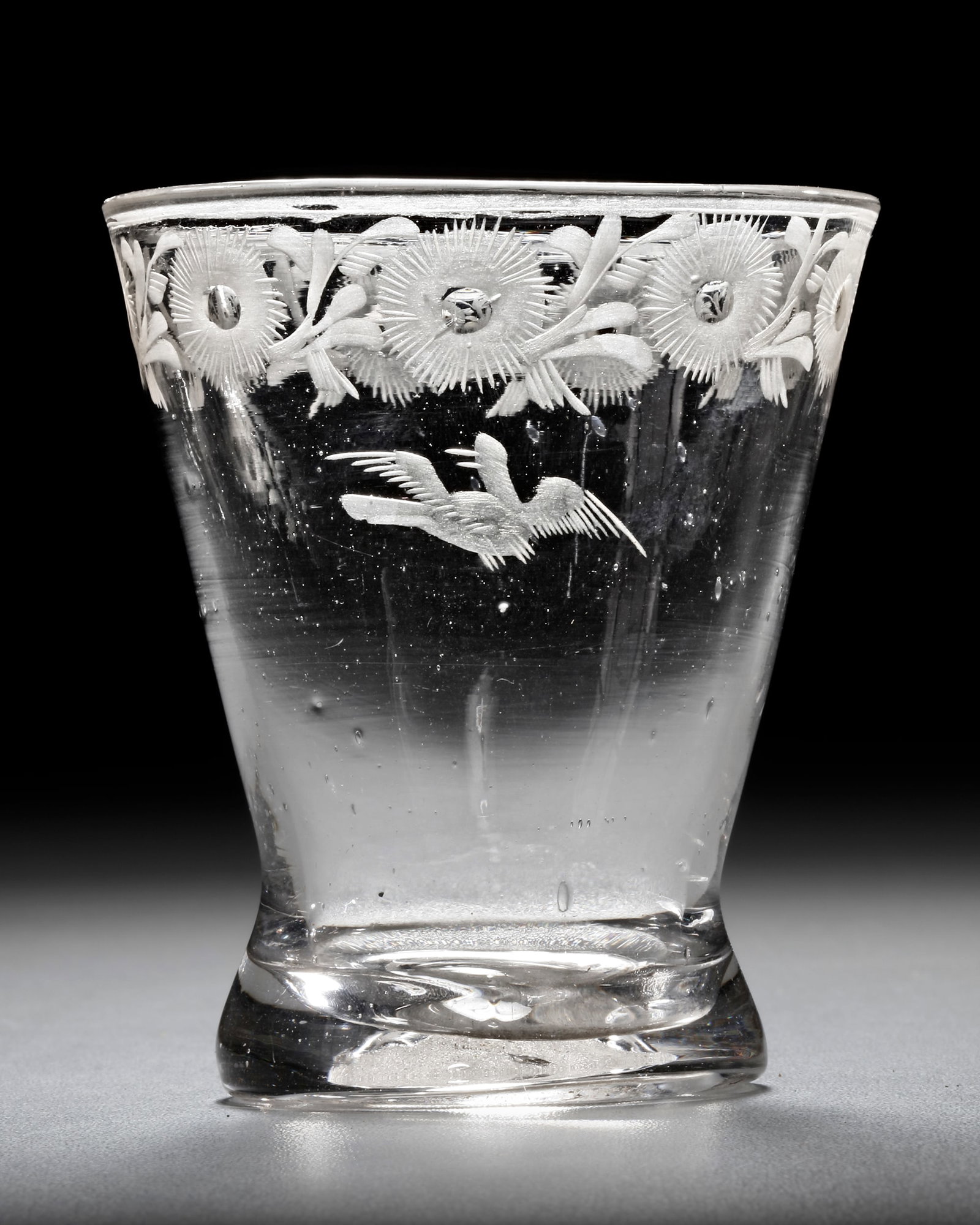 A DUTCH 18TH CENTURY CRYSTAL ENGRAVED FOOLING GLASS OR 'FOPGLAS': Engraved with a flower band to the rim and with a bird. Height 9 cm.A fooling glass ('fopglas' in Dutch) has several holes in the rim (hidden in the flower engravings) of the glass. If used the wine w