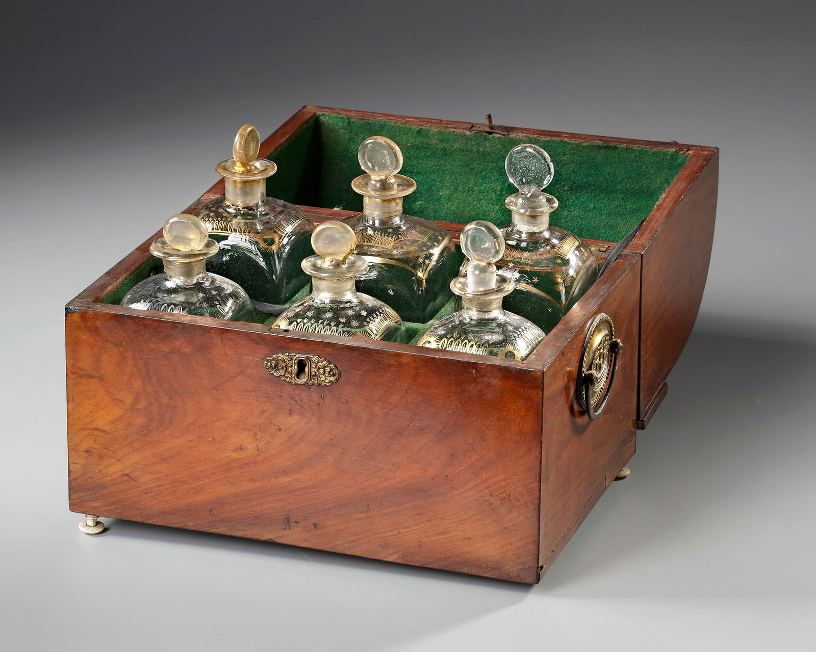 A DUTCH MAHOGANY LIQUOR CABINET, EARLY 19TH CENTURY: Of rectangular form with domed hinged cover, opening to a felt lined interior and 6 parcel gilt glass decanters. The sides with brass handles and on bone bun feet (one missing). Dimensions: h. 24.5 cm