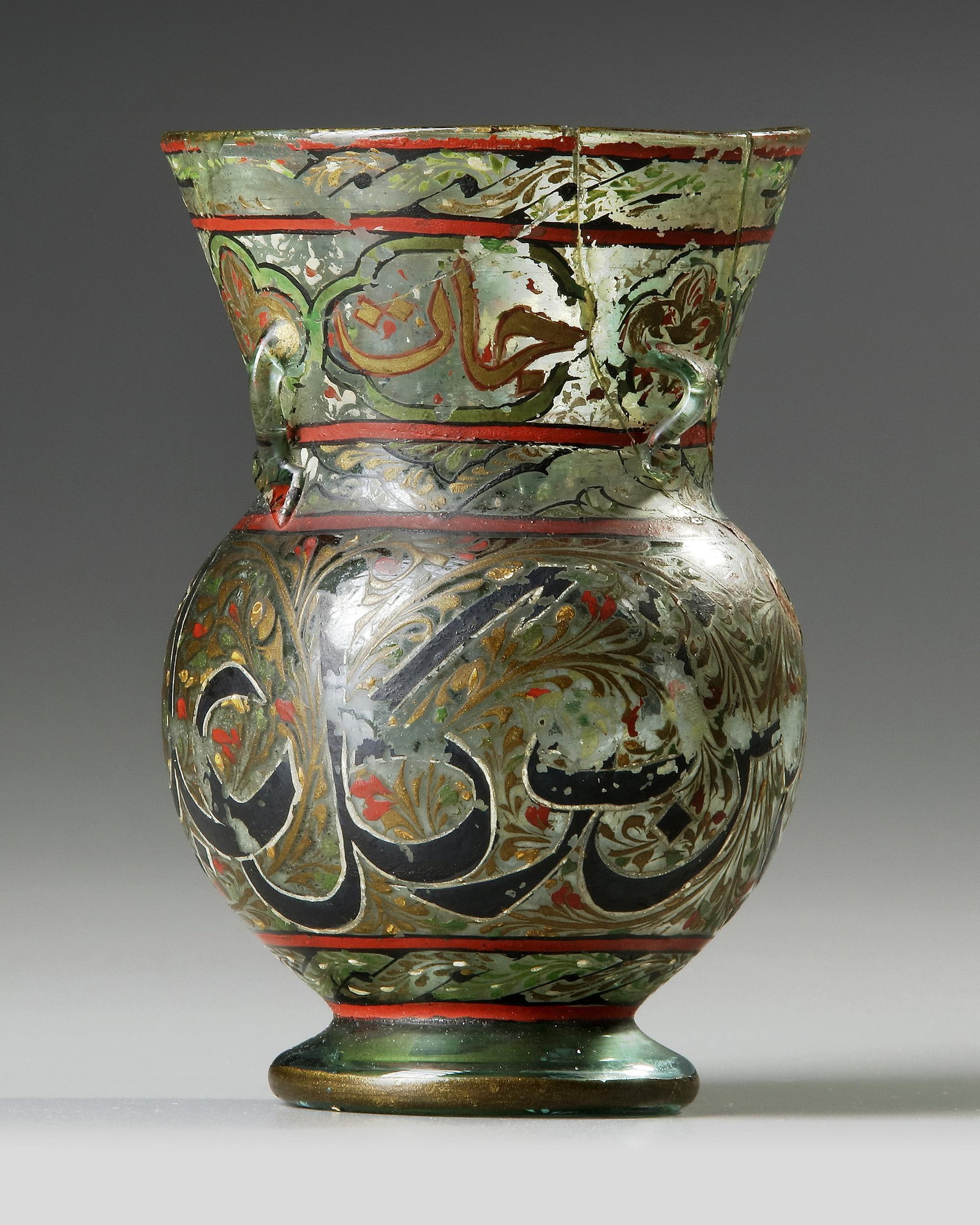 ENAMELED AND GILDED CLEAR GLASS MOSQUE LAMP, 17TH-18TH CENTURY: Of typical form, the rounded angled body with flaring conical mouth on short foot, three applied loop handles around the body. Height: 13 cm. Diameter: 9 cm. Provenance: a private collection, Germany
