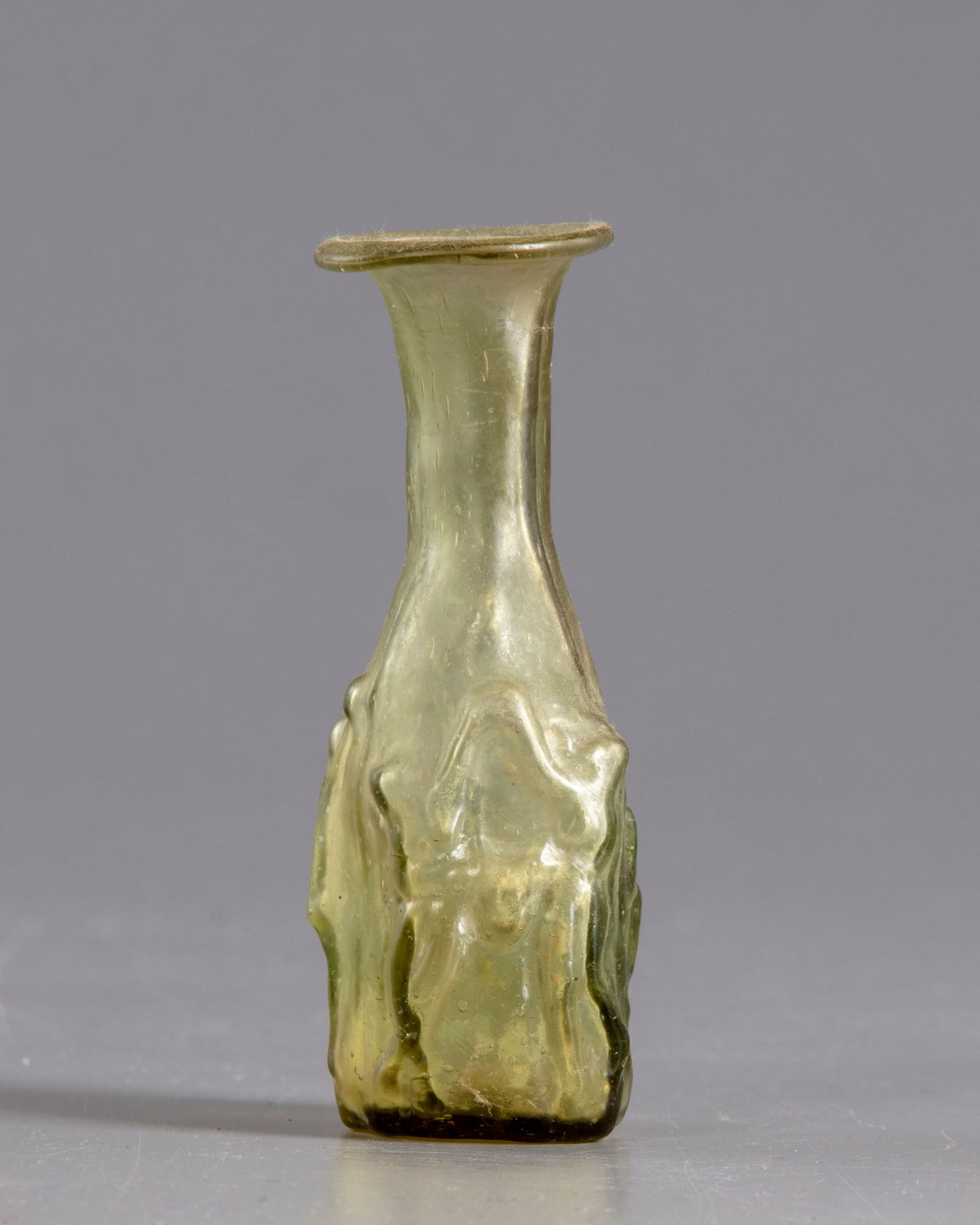 A ROMAN GLASS FLASK, CIRCA 3RD CENTURY AD: A nice translucent green mould-blown flask, depicting a man and woman in erotic scene, The flask has a short cylindrical neck with an everted rounded rim, with a slightly concave base. Height 11 cm. P