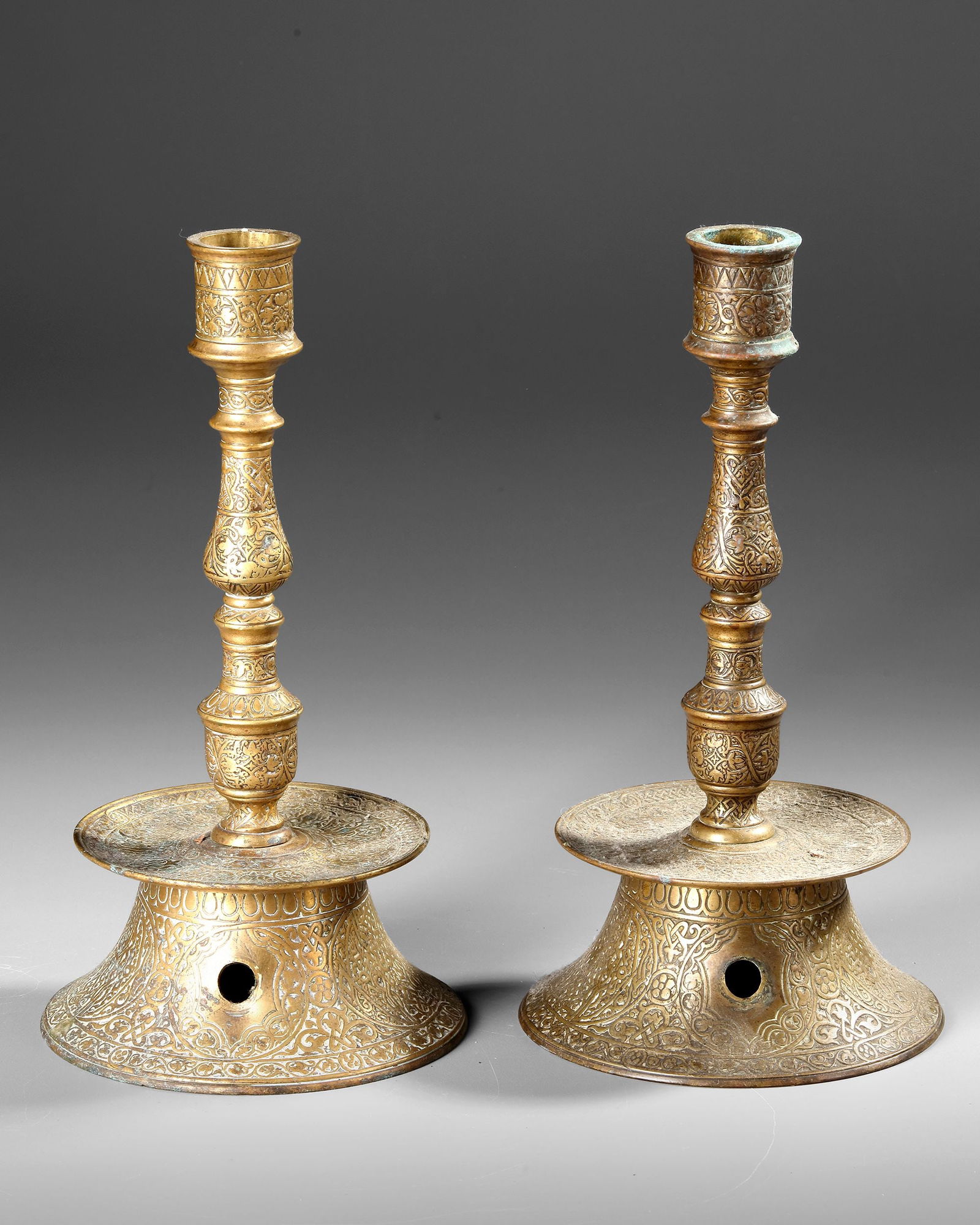 TWO OTTOMAN ENGRAVED BARASS CANDLESTICKS , TURKEY 17TH CENTURY: Elegant Ottoman brass candlesticks, finely engraved with floral and arabesque motifs, featuring flared bases and slender decorative stems H. 25 cm.
