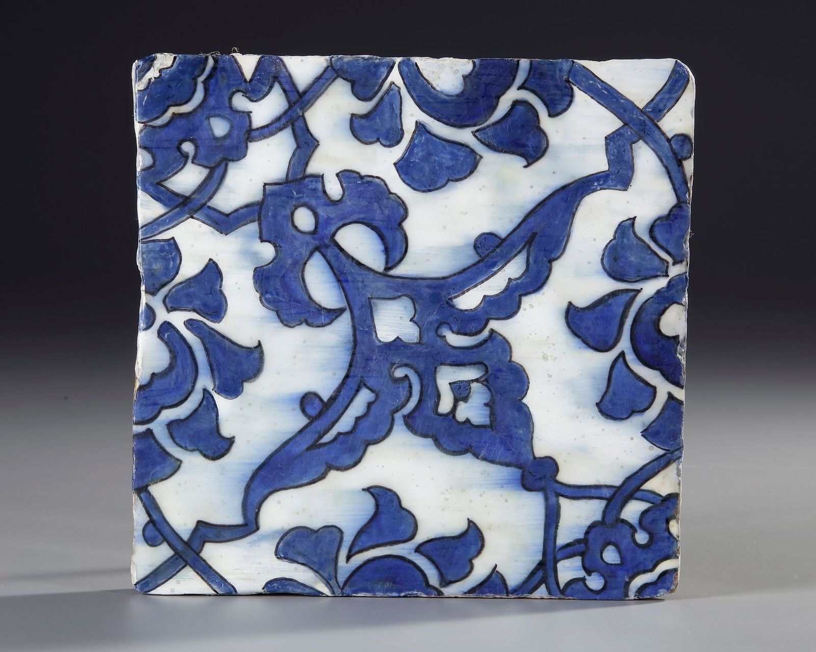 A 'DOME OF THE ROCK' POTTERY TILE, JERUSALEM, MID-16TH CENTURY: Of square form, decorated in cobalt blue with black outlines on a white ground with a stylised split-palmette and lotus motif under a transparent glaze. 19.6 cm. square