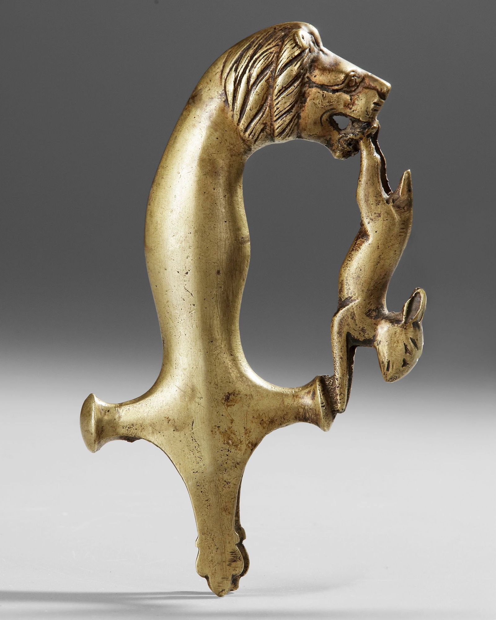 A MUGHAL SWORD HILT, INDIA, 19TH CENTURY: This finely crafted Mughal sword hilt, dating to the 19th century, is cast in gilt bronze and shaped as a lion attacking a hare. ca. 18 by 9 cm.