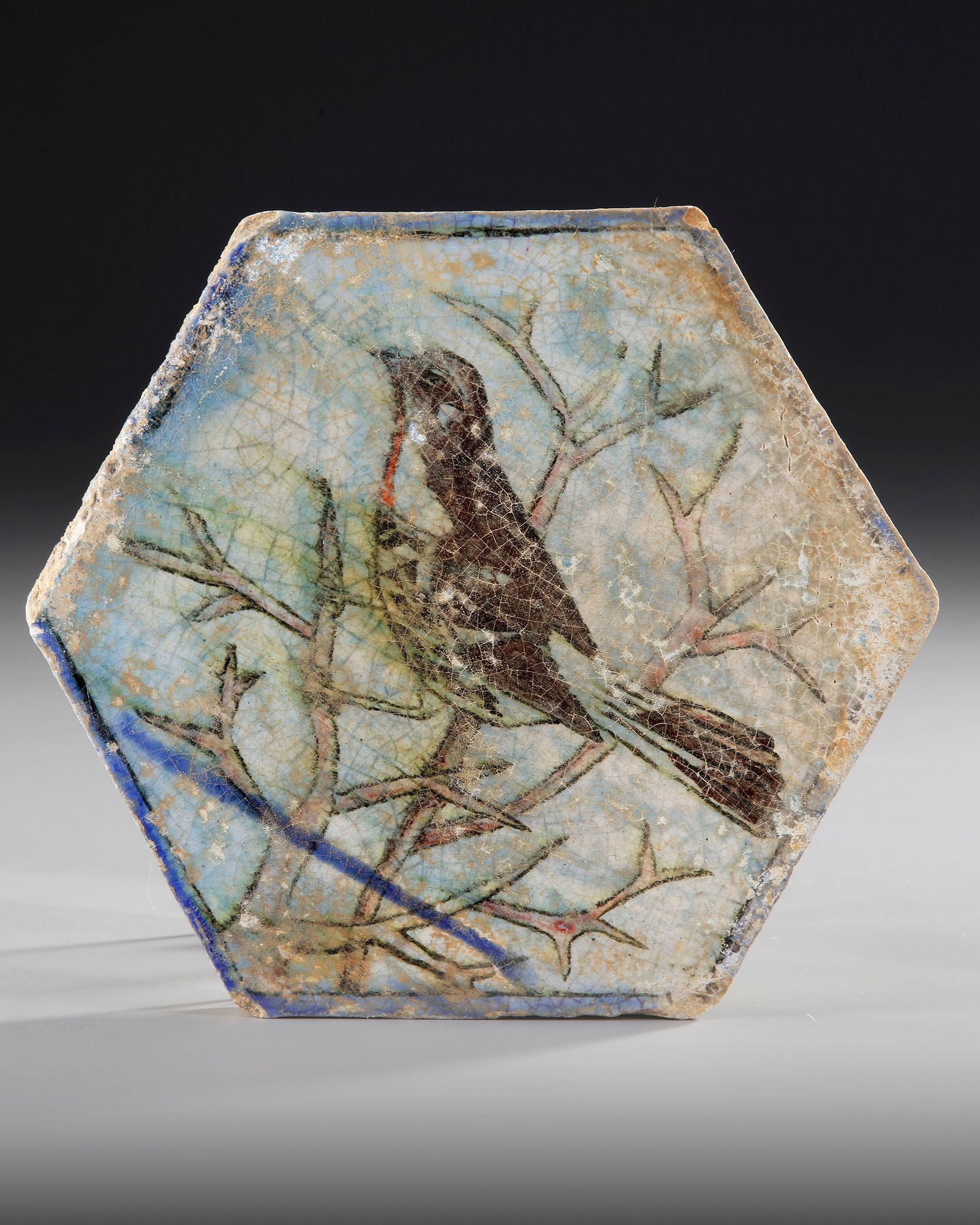 A PERSIAN TILE, QAJAR PERIOD, 19TH CENTURY: A finely crafted hexagonal Persian ceramic tile from the Qajar period (19th century), decorated with the image of a bird perched on branches. 20 by 22.5 cm.