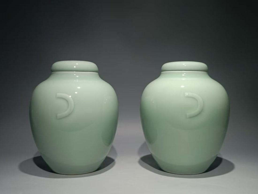 A PAIR OF CHINESE CELADON-GLAZED JARS AND COVERS: A pair of Chinese porcelain jars, each with a tapering ovoid body with a high gently rounded shoulder, with two crescent-shaped handles to each side of the body, covered overall in an even pale celado