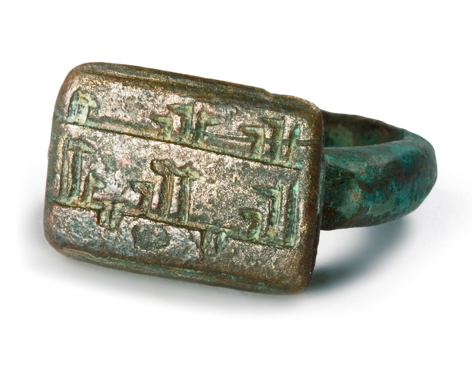 AN ISLAMIC KUFIC INSCRIBED BRONZE RING: A bronze ring with rectangular shaped top engraved with Arabic kufic inscription. 1st/2nd AH-7th/8th AD century
