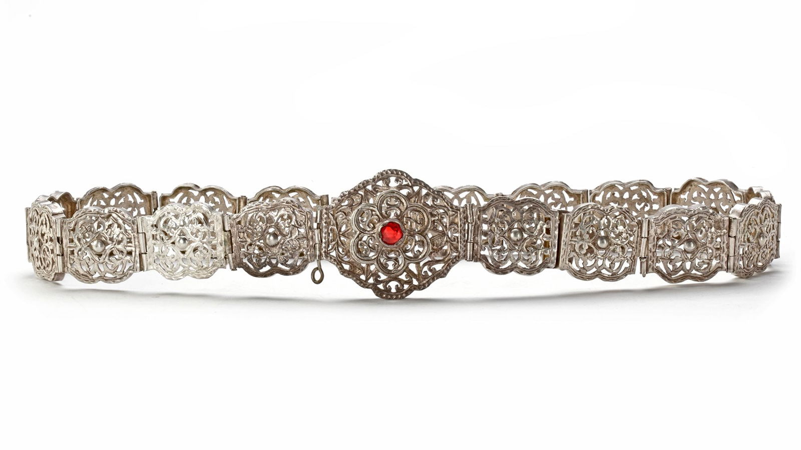 AN OTTOMAN SILVER BELT, 19TH CENTURY: An ornate 19th-century Ottoman silver belt, composed of intricately pierced floral panels linked together. The central clasp features a rosette design set with a vivid red glass stone, showcasing fine