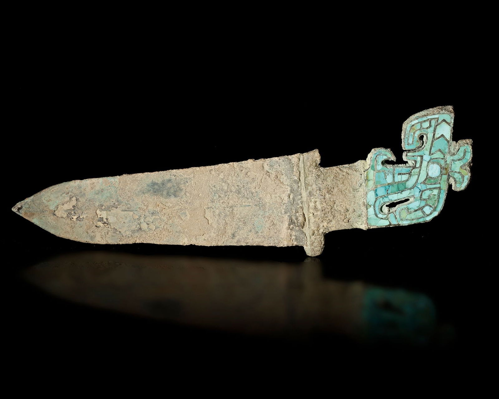 A TURQUOISE-INLAID DAGGER, LATE SHANG DYNASTY: An ancient Chinese dagger from the Late Shang dynasty featuring a bronze blade and a finely decorated hilt inlaid with turquoise stones forming a stylized mythical motif. Such weapons combined ritual