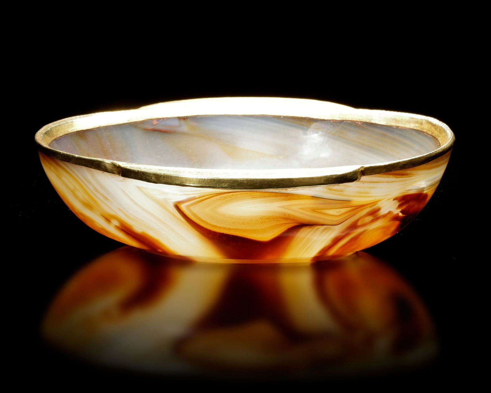 A HAN DYNASTY AGATE EAR-CUP (206 BCE â€“ 220 CE): Banded agate with gilt metal rimA finely carved agate ear-cup, shaped in the elegant oval form characteristic of early Chinese ritual drinking vessels. The cup displays beautiful natural banding in wa