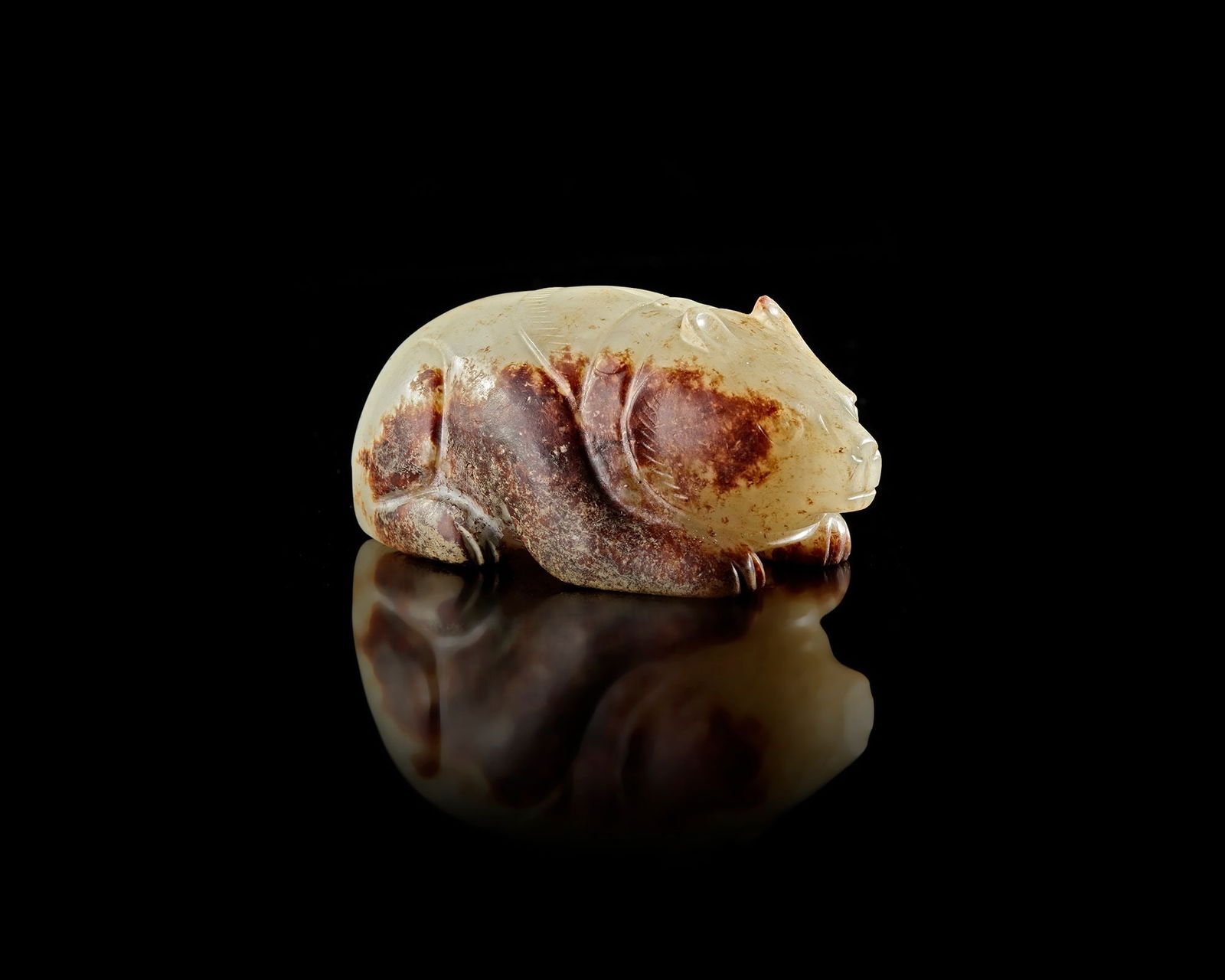 A JADE BEAR, CHINA, SONG DYNASTY (960â€“1279): A finely carved jade bear sculpture crafted from grey jade with natural brown inclusions. The animal is depicted in a calm resting posture, with softly rounded forms and delicate incised details defin