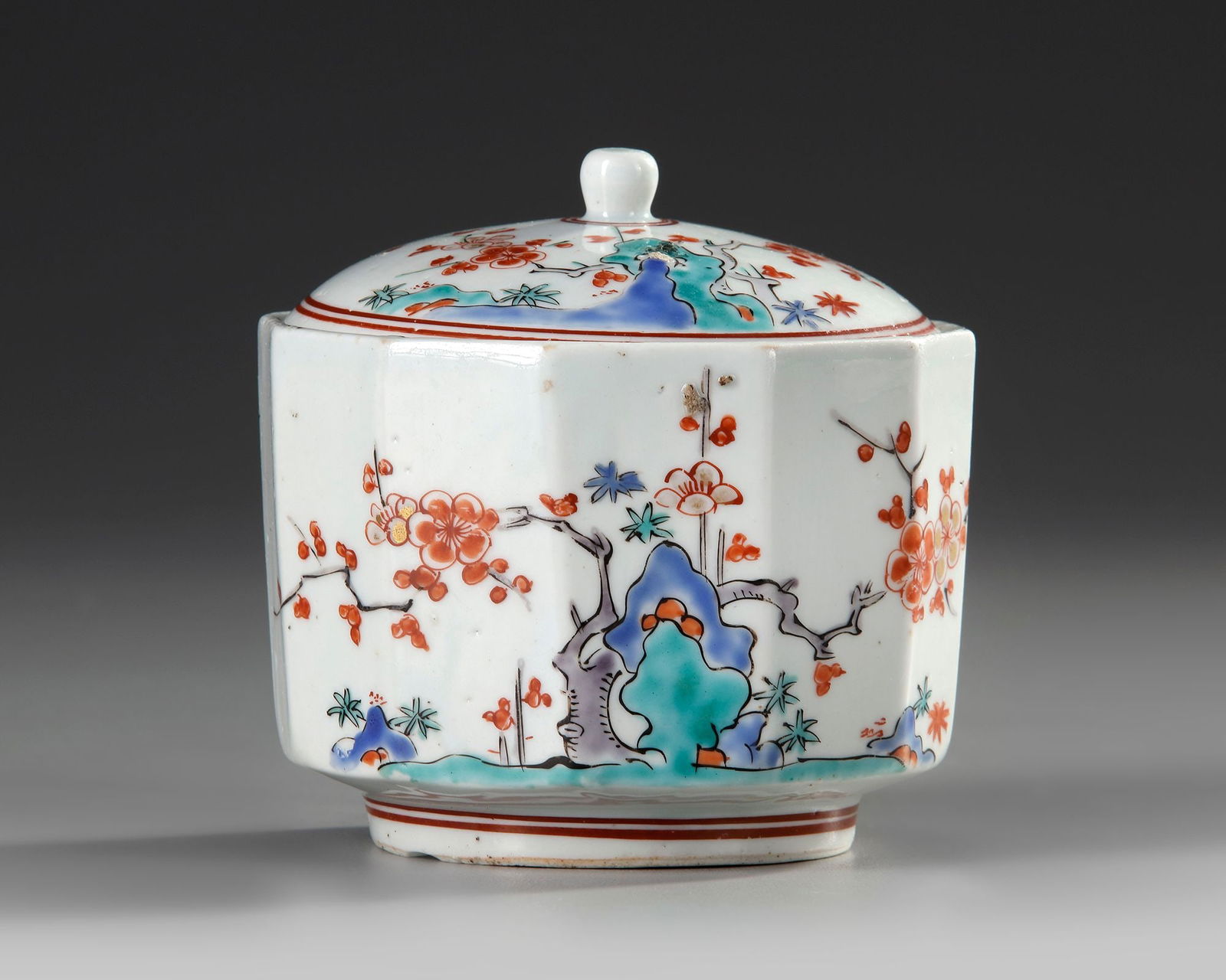 A JAPANESE PORCELAIN KAKIEMON POT WITH COVER, EDO PERIOD, 18TH CENTURY: A Japanese porcelain twelve sided pot with cover, brightly enameled in blue, turquoise and red enamels with the Kakiemon pattern of a blossoming pine branches growing from ornamental rocks. Height 9.5