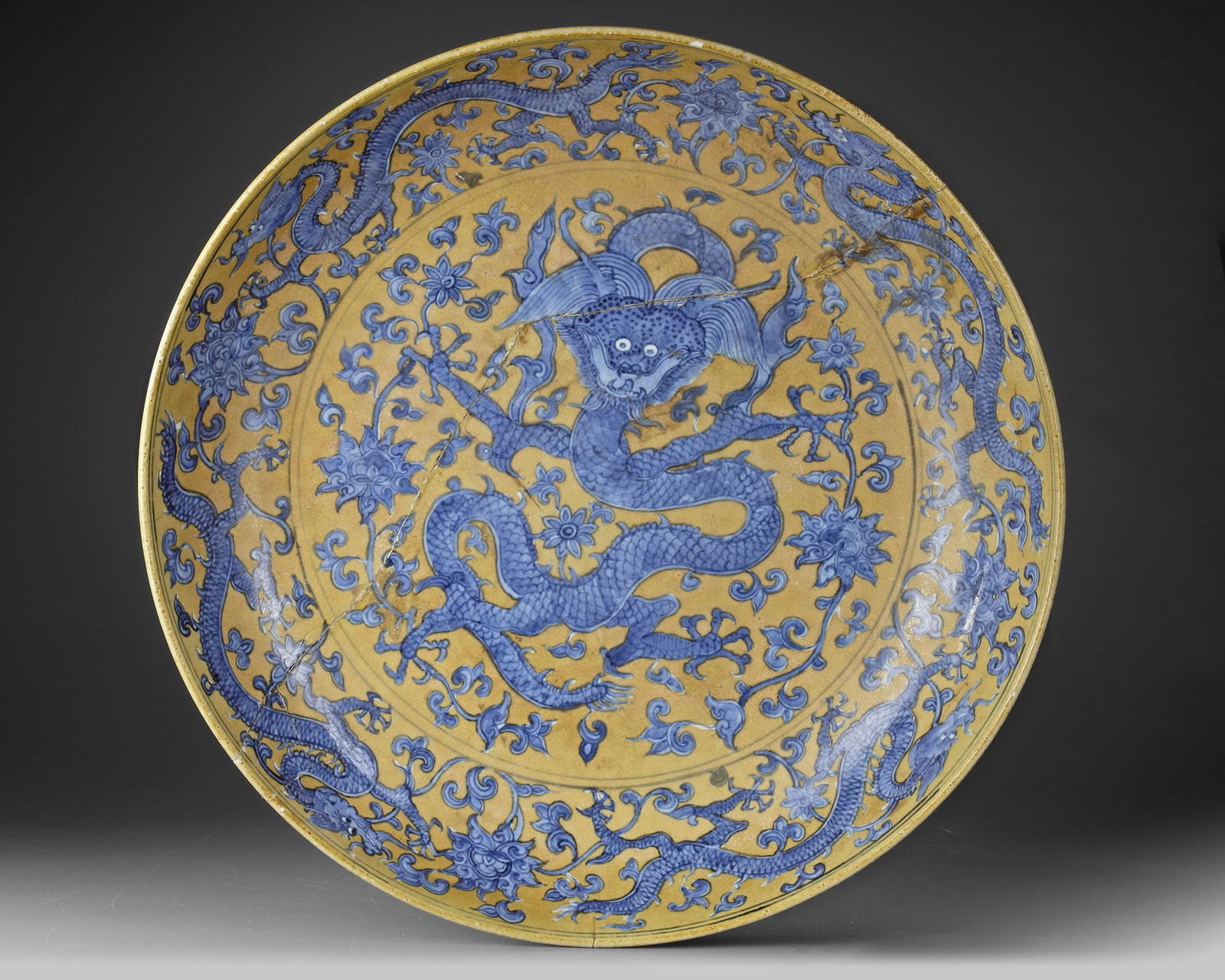 A LARGE CHINESE BLUE-ENAMELED AND YELLOW-GROUND 'DRAGON' CHARGER: A Chinese porcelain charger, the low rounded sides rising from a tapered foot, finely enameled in bright tones of blue against a rich yellow ground. The center is decorated with a ferocious five-clawe