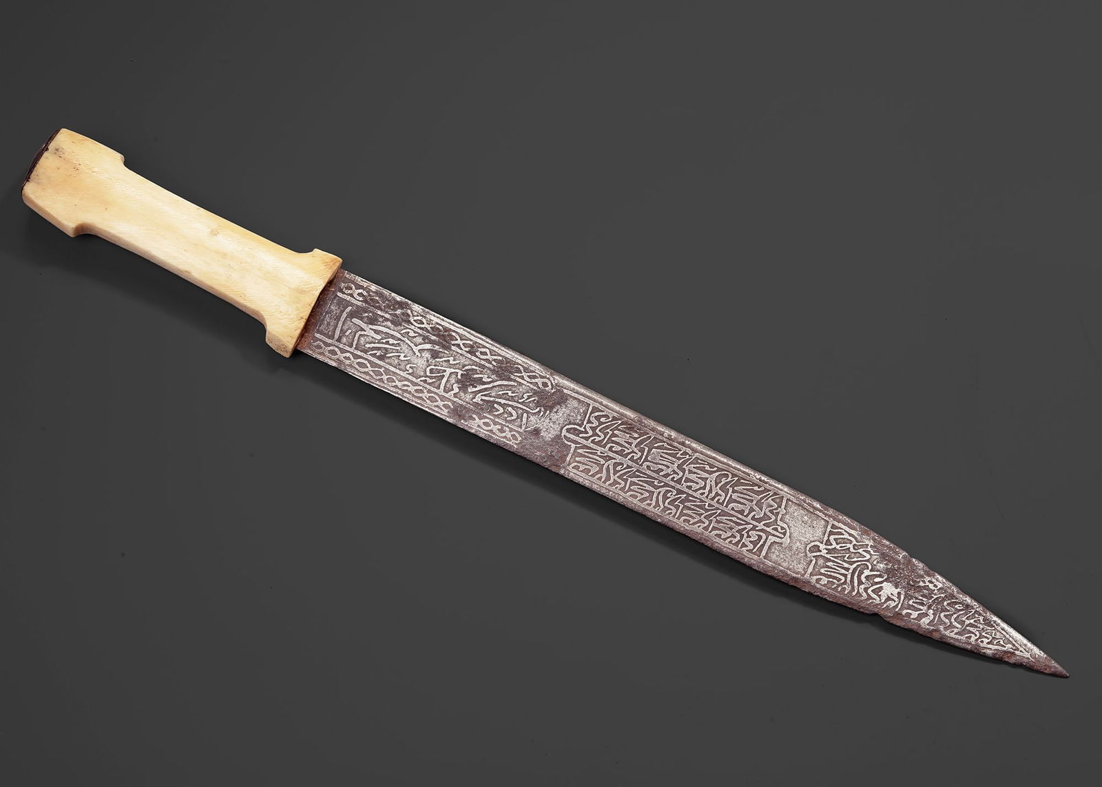 A PERSIAN DAGGER WITH BONE HANDLE, QAJAR PERIOD, 19TH CENTURY: Persian dagger, likely from the Qajar period, featuring a carved bone handle and a steel blade richly engraved with Islamic calligraphy and decorative motifs. L. 46 cm.256 gr.