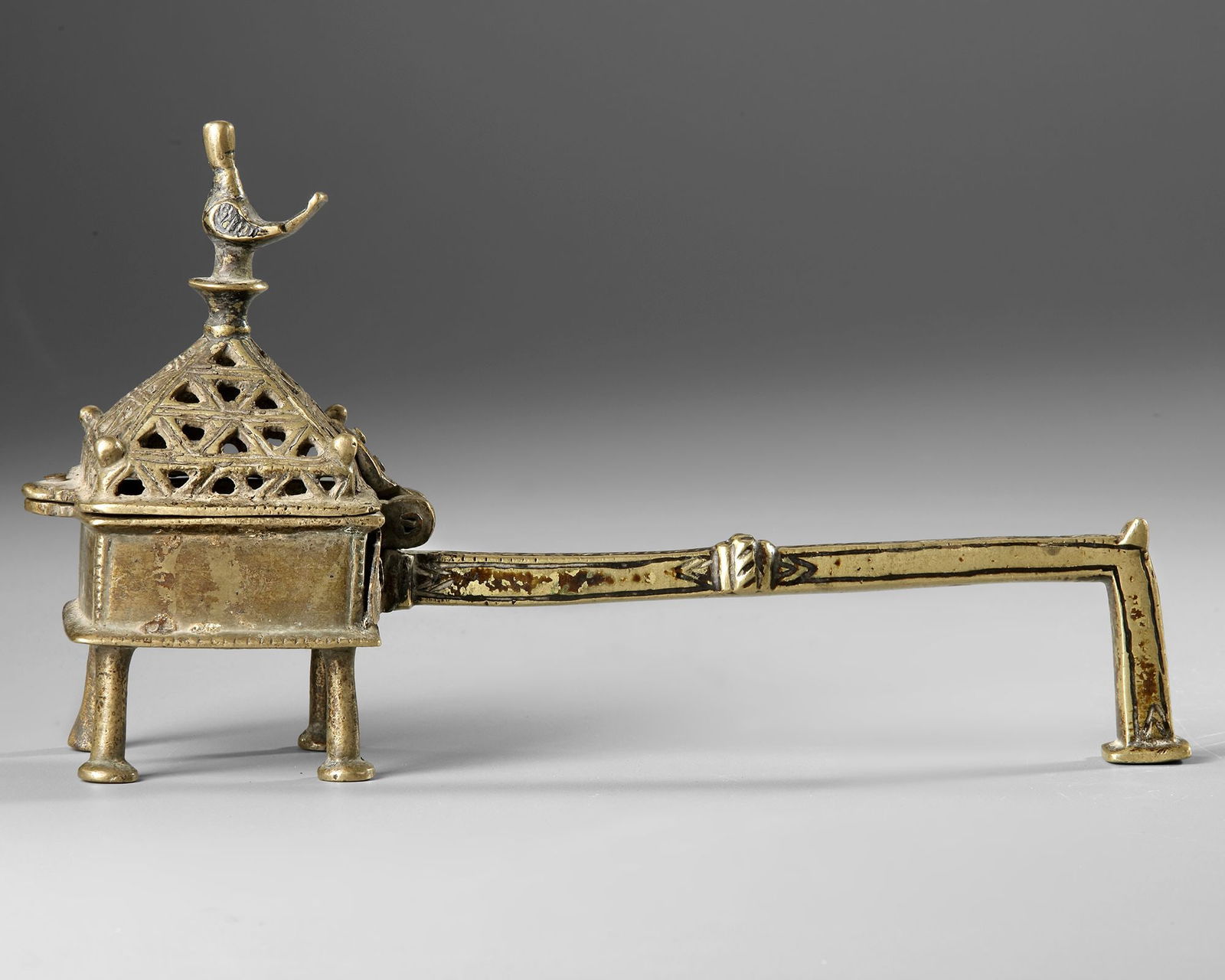 AN INCENSE BURNER YEMEN, 15TH CENTURY: A finely cast 15th-century Yemeni incense burner in brass, raised on four slender legs and fitted with a long handle for safe handling. The rectangular body is surmounted by a pierced pyramidal lid de