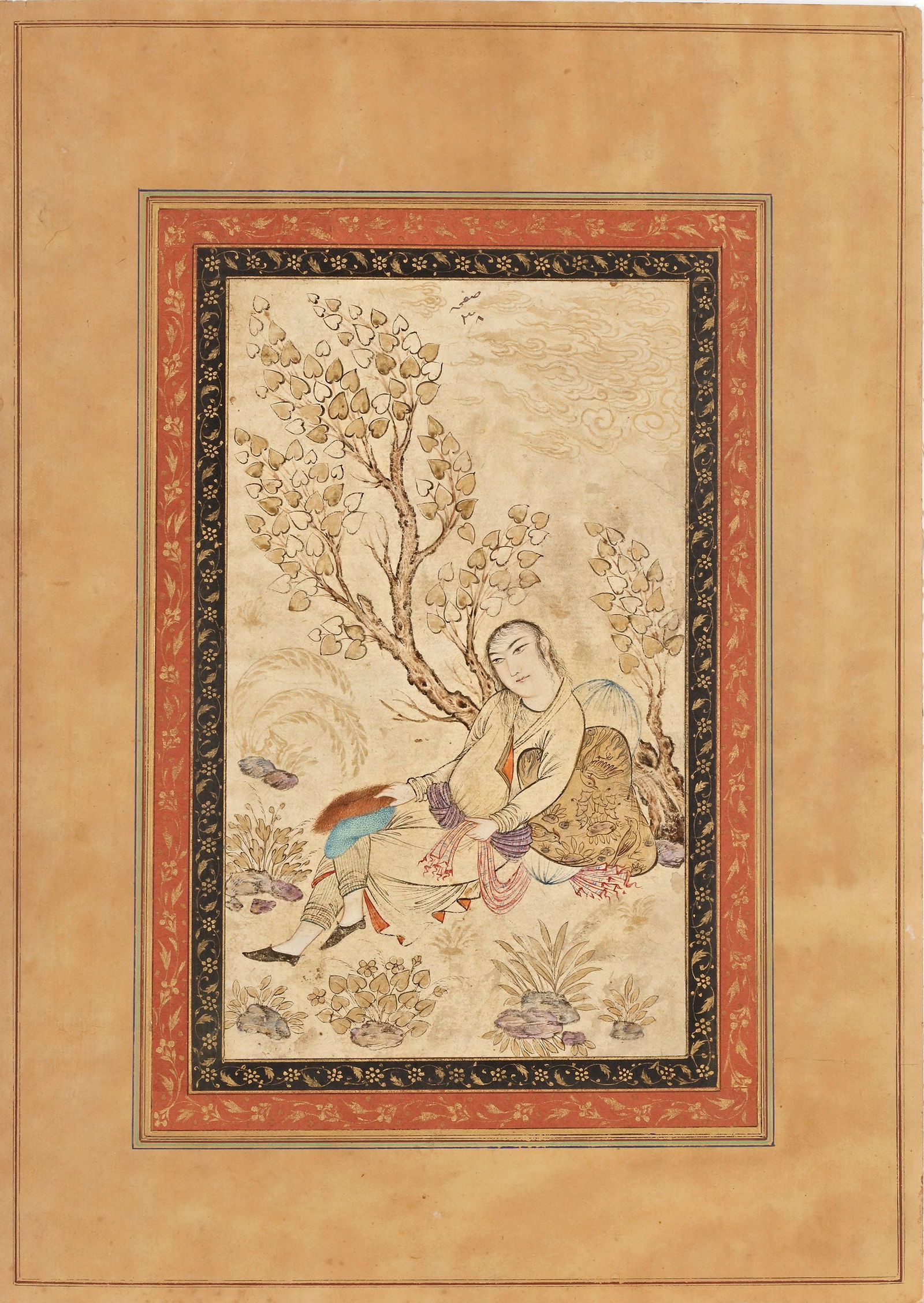A YOUTH RECLINING BENEATH A TREE, PERSIA QAJAR, 19TH CENTURY: Opaque pigments heightened with gold on paper, set within double inner borders decorated with gilt floral scrolls on polychrome grounds, mounted on card.The painting depicts a youthful figure reclinin