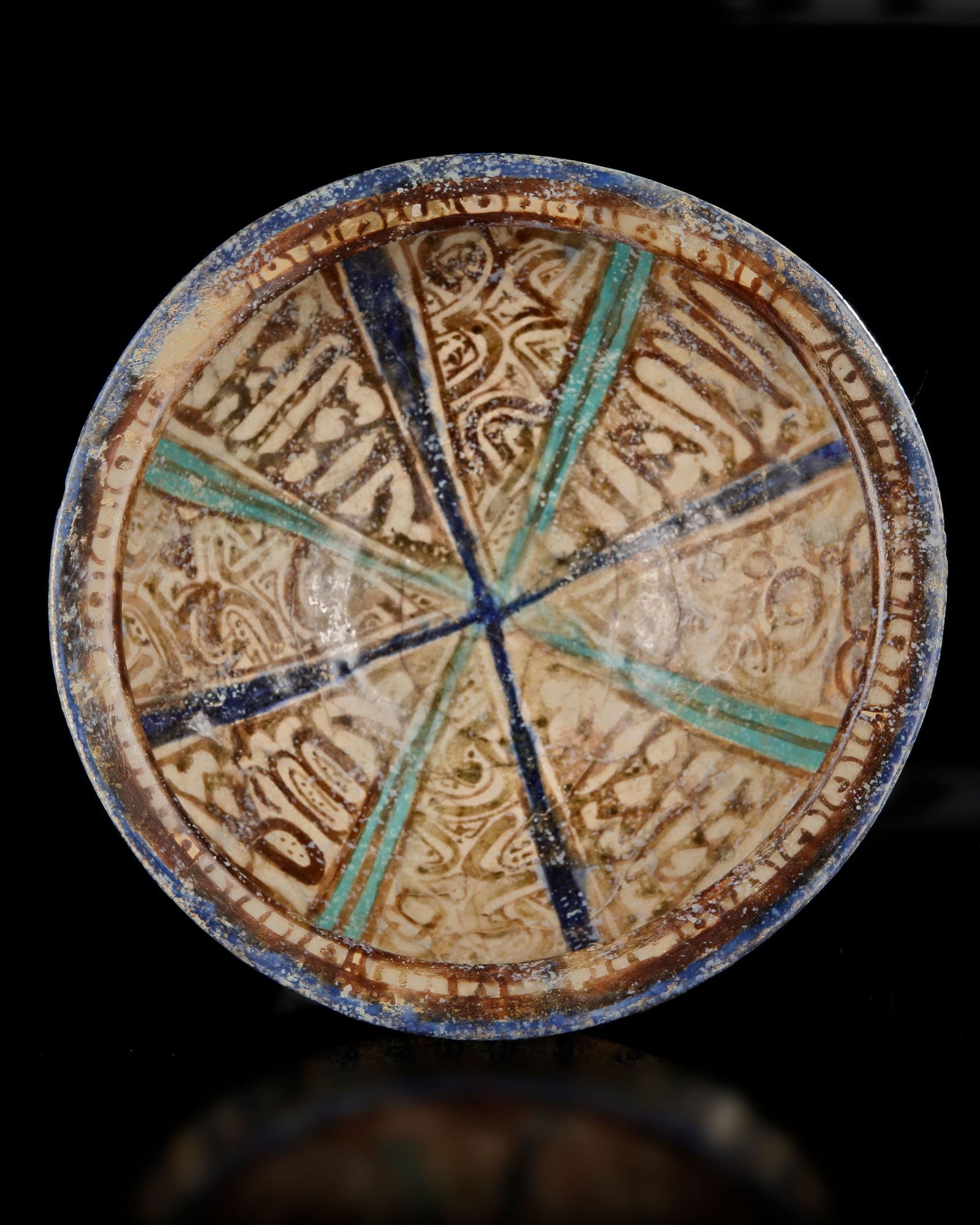 A KASHAN POTTERY BOWL, PERSIA 12TH CENTURY: A Persian pottery bowl on a small foot ring with gently flaring sides and a slightly thickened rim. The interior is organized in a radial composition of wedge-shaped panels converging at the center, d