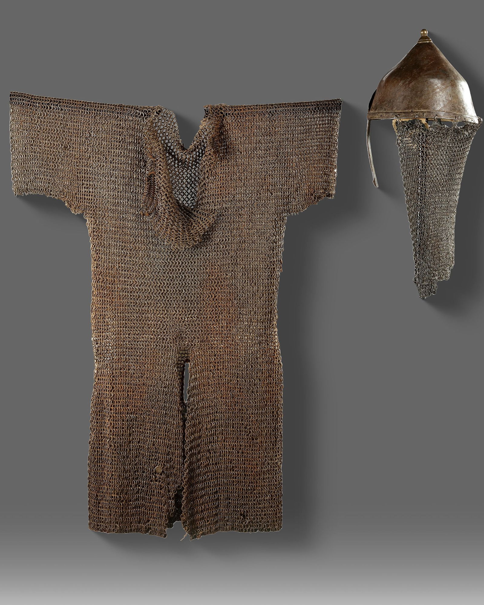 CHAINMAIL AND HELMET YEMEN, 15TH CENTURY: A rare 15th-century Yemeni chainmail shirt accompanied by a conical steel helmet with attached mail aventail. The finely linked rings form a flexible yet durable defensive garment, while the helmetâ&