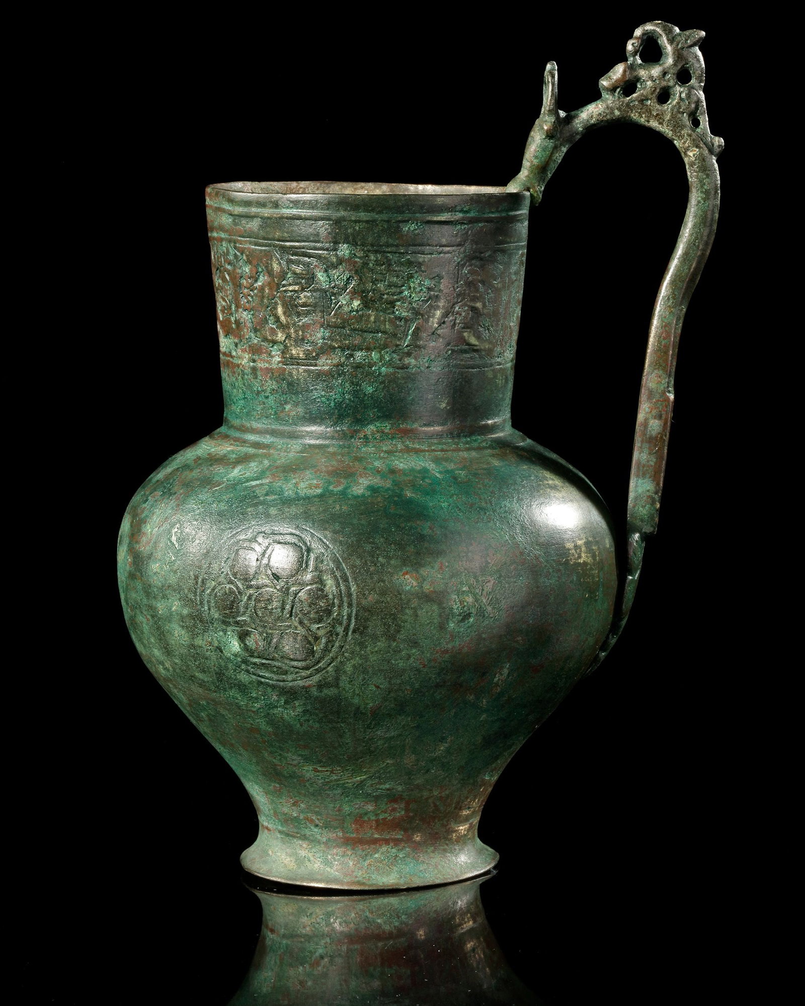 A SELJUK ENGRAVED BRONZE EWER, 12TH CENTURY: A finely crafted Seljuk bronze ewer from the 12th century, distinguished by its elegant pear-shaped body and tall cylindrical neck. The surface is richly engraved with decorative bands featuring styli