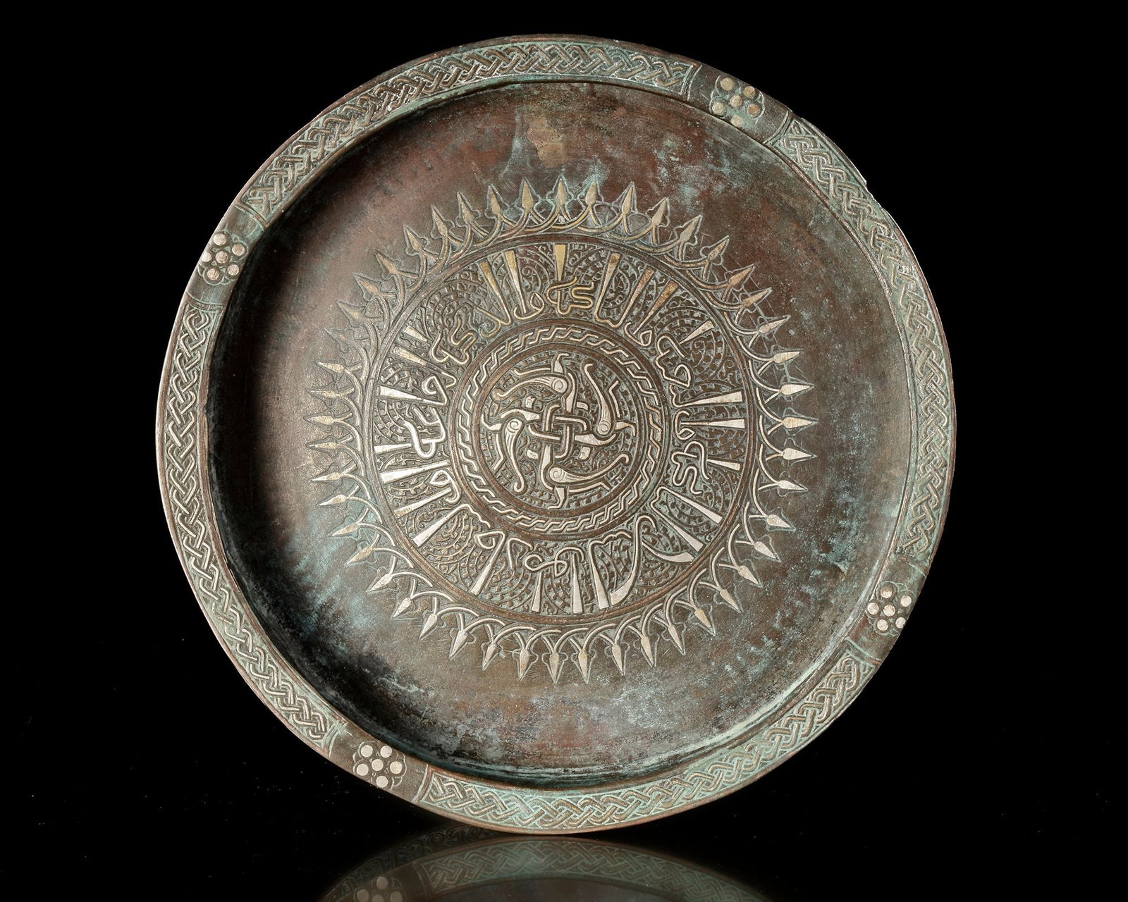 A KHORASSAN SILVER INLAID BRONZE TRAY, PERSIA, 11TH CENTURY: A finely crafted bronze tray enriched with silver inlay, featuring a central medallion surrounded by dense geometric and calligraphic decoration. the broad rim is adorned with interlacing motifs, refl