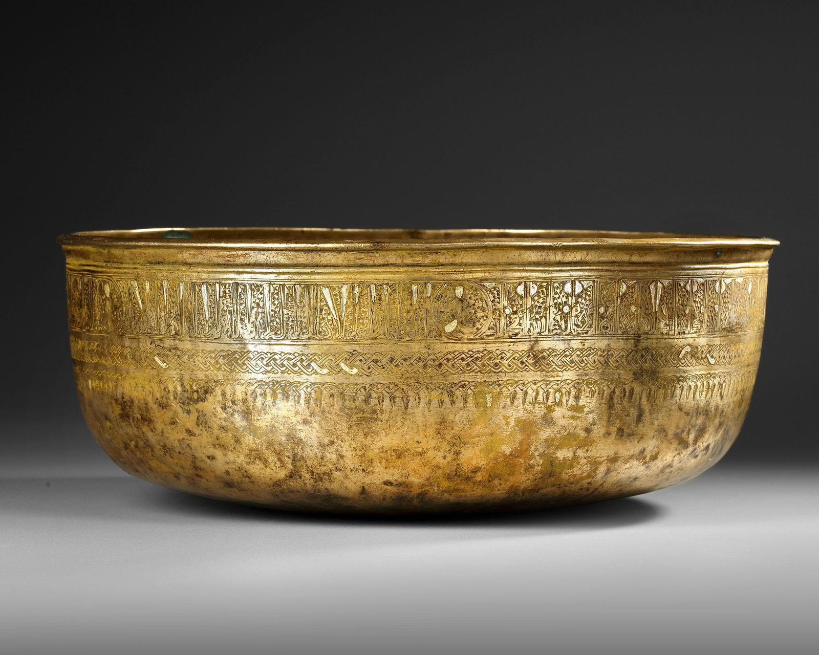 A LARGE AYYUBID SILVER INLAID BRASS BOWL WITH INSCRIPTIONS, EGYPT OR SYRIA, 13TH CENTURY: A large bowl of deep rounded form decorated around the rim with an elegant benedictory inscription separated by six roundels, each containing a silver inlaid seated figure surrounded by small florets