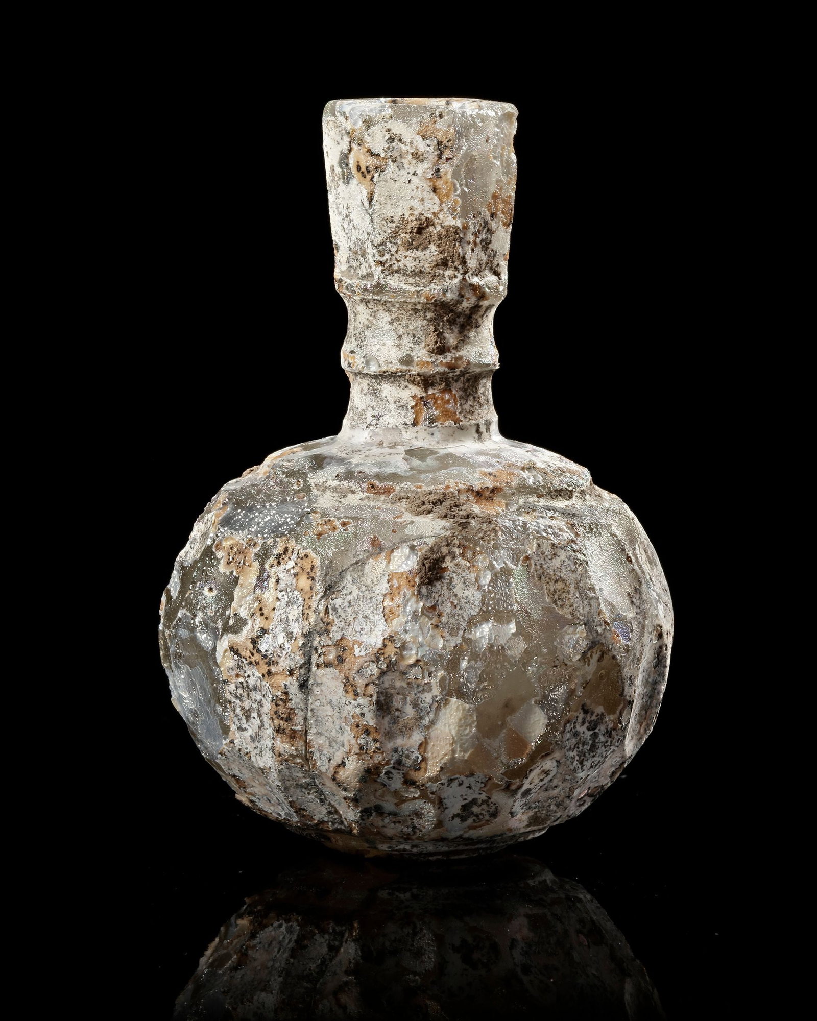 A WHEEL-WHEEL-CUT CLEAR GLASS BOTTLE NORTH EAST PERSIA, 9TH-10TH CENTURY: With spherical body and slightly flaring faceted neck, the body with a band of two rows of wheel-cut roundels bordered by concentric, some surface encrustation. 10 cm high.