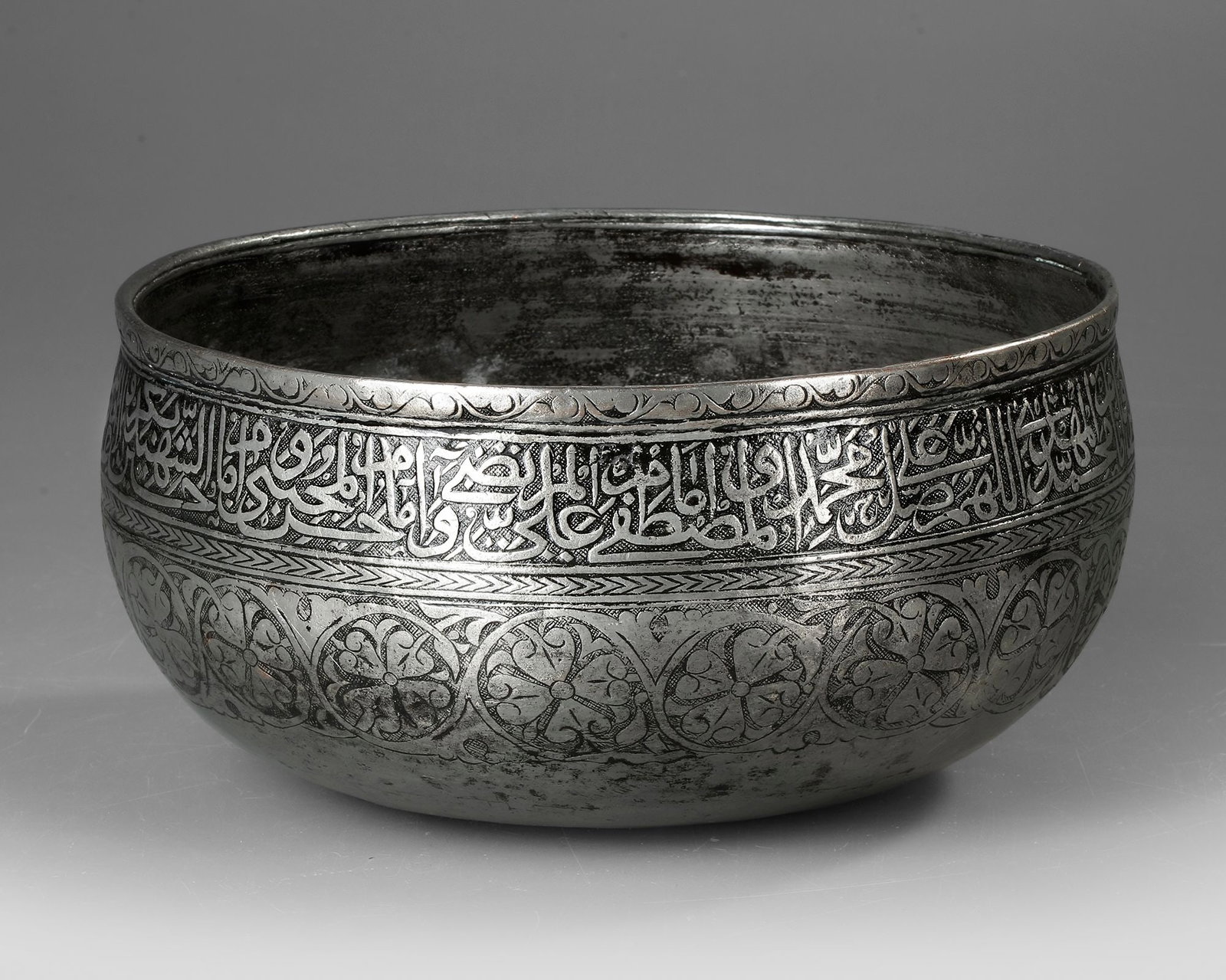 A TIMURID ENGRAVED METAL BOWL, 14TH CENTURY: A refined Timurid-period metal bowl dating to the 14th century, finely engraved with elegant Arabic calligraphy around the rim and scrolling vegetal motifs across the body. Diameter. 23 cm. High. 12 c
