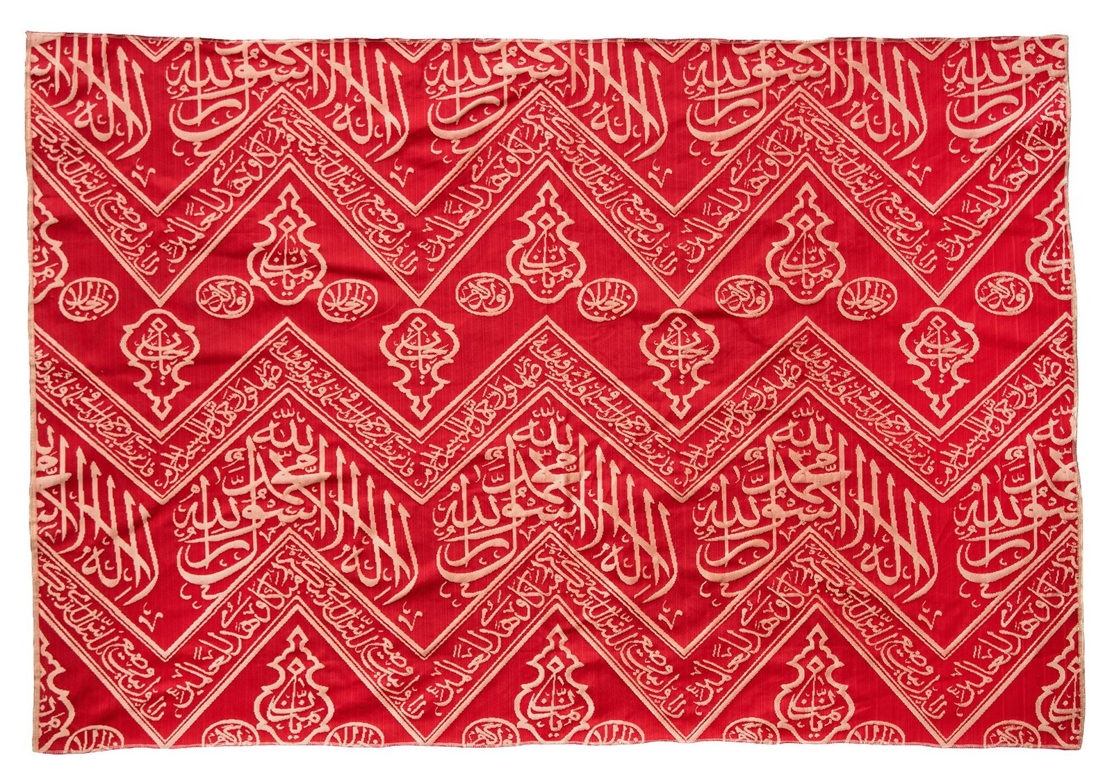 AN OTTOMAN RED EMBROIDERED SILK KISWA FRAGMENT, TURKEY OR EGYPT 20TH CENTURY: A fragment from the inner curtain of the sacred kiswa that lines the interior wall of the Kaaba, woven in cream-colored silk against a rich dark red background. The design features chevron patterns in