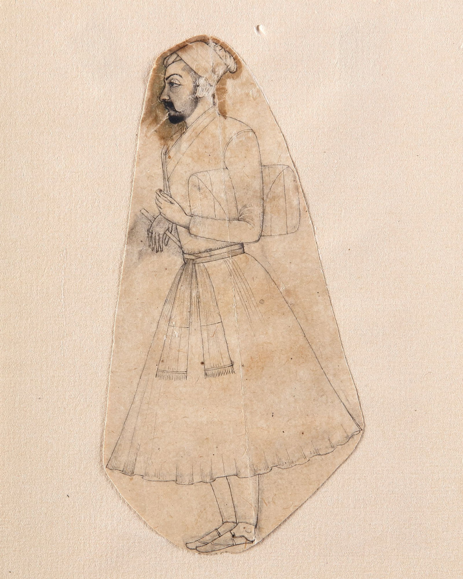 A STANDING MALE FIGURE, INDIA CA.1720: Ink on paper, depicting a refined ink study of a turbaned man shown in left profile, wearing a long jama secured with a sash and soft pointed shoes. The figure, likely a courtier or attendant, is rend