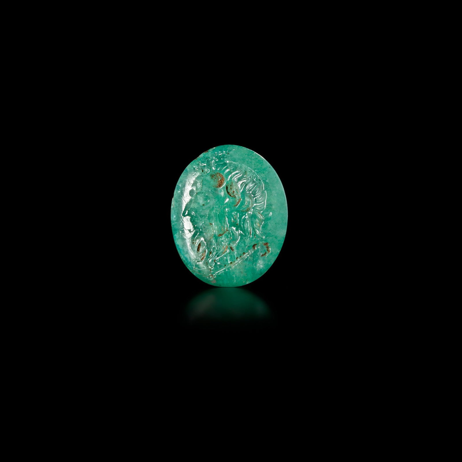 ROMAN EMERALD INTAGLIO OF SILENUS 1ST CENTURY A.D.: This exquisite Roman intaglio, masterfully carved in vibrant emerald, portrays the expressive visage of Silenusâ€”the wise, bearded companion of Dionysus. Revered in Greco-Roman mythology