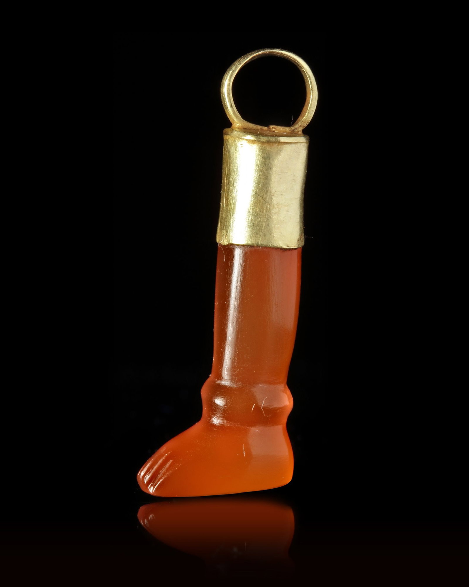 A CARNELIAN AMULET/SEAL IN THE SHAPE OF A LEG, CIRCA 700 BC: A carnelian amulet in the shape of a lower leg. On the sole of the foot there are five Aramaic/Phoenician letters. The leg is mounted in a gold cap with a suspension hoop. with Aramaic letters 28 mm.