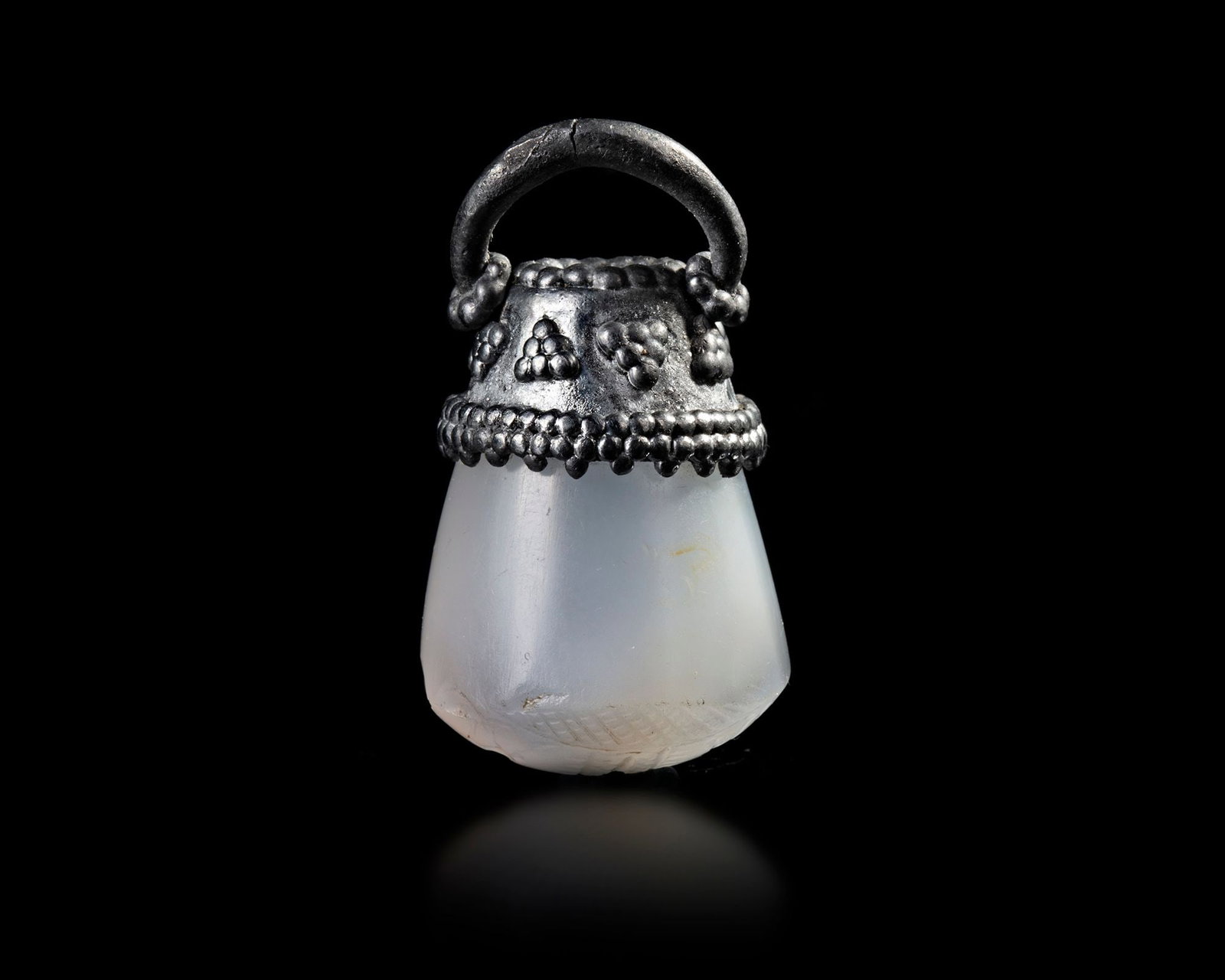 A NEO-ASSYRIAN STAMP SEAL IN BLUE CHALCEDONY, 7TH CENTURY BC: A Neo-Assyrian stamp seal with a silver filigreed suspension mount. The seal shows two bull-men holding up a winged solar disc, the stand upon an exergal line, below which is cross hatched. A sacred s